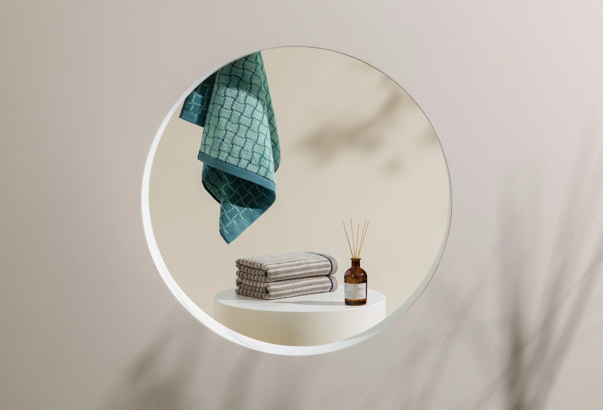 Still life featuring folded towels and diffuser arranged within circular wall opening, set build and props styling by Steffi Bühlmaier, photography by Michael Tewes, creative direction by Studio Kühn for Möve, 2025