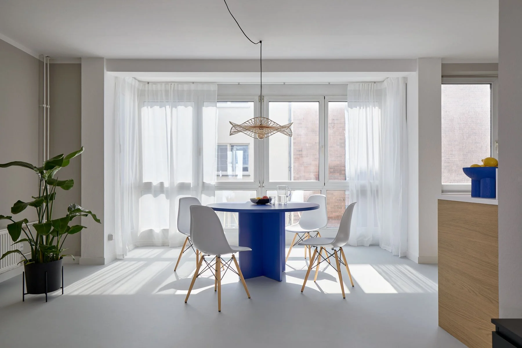 Bright dining area with blue table, white chairs and sheer curtains, apartment in Berlin Mitte, interior design, Innenausbau and styling by Steffi Bühlmaier, photography by Tobias Bärmann, 2024