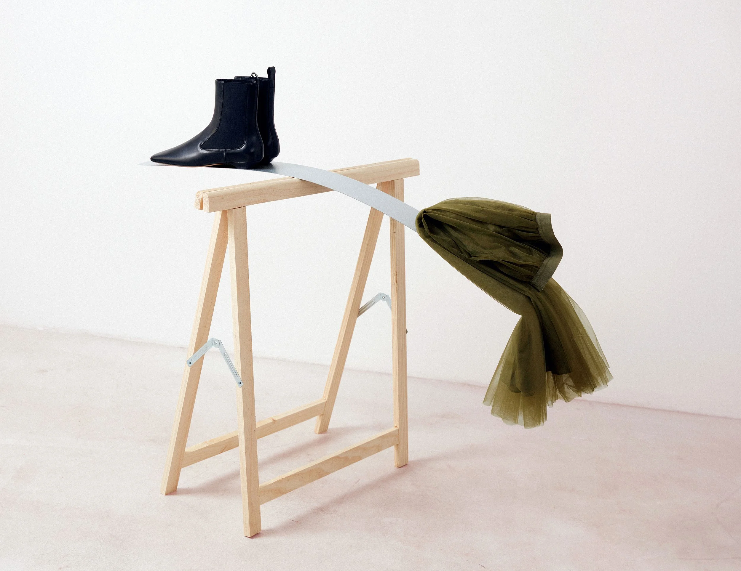 Fashion still life with black ankle boots balanced on wooden stand and green tulle garment, art direction and set design by Steffi Bühlmaier, photography by Jessica Grossmann for Heyday Magazine, 2022