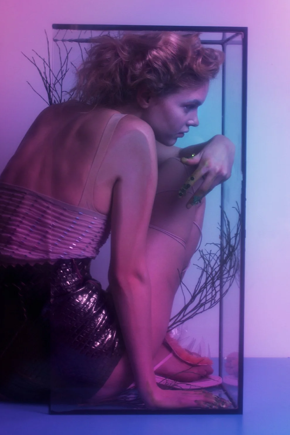 Editorial fashion image featuring a model trying to fit into an aquarium in soft coloured light, set design and props styling by Steffi Bühlmaier, photography by Loreen Hinz for Vision Magazine China, 2019