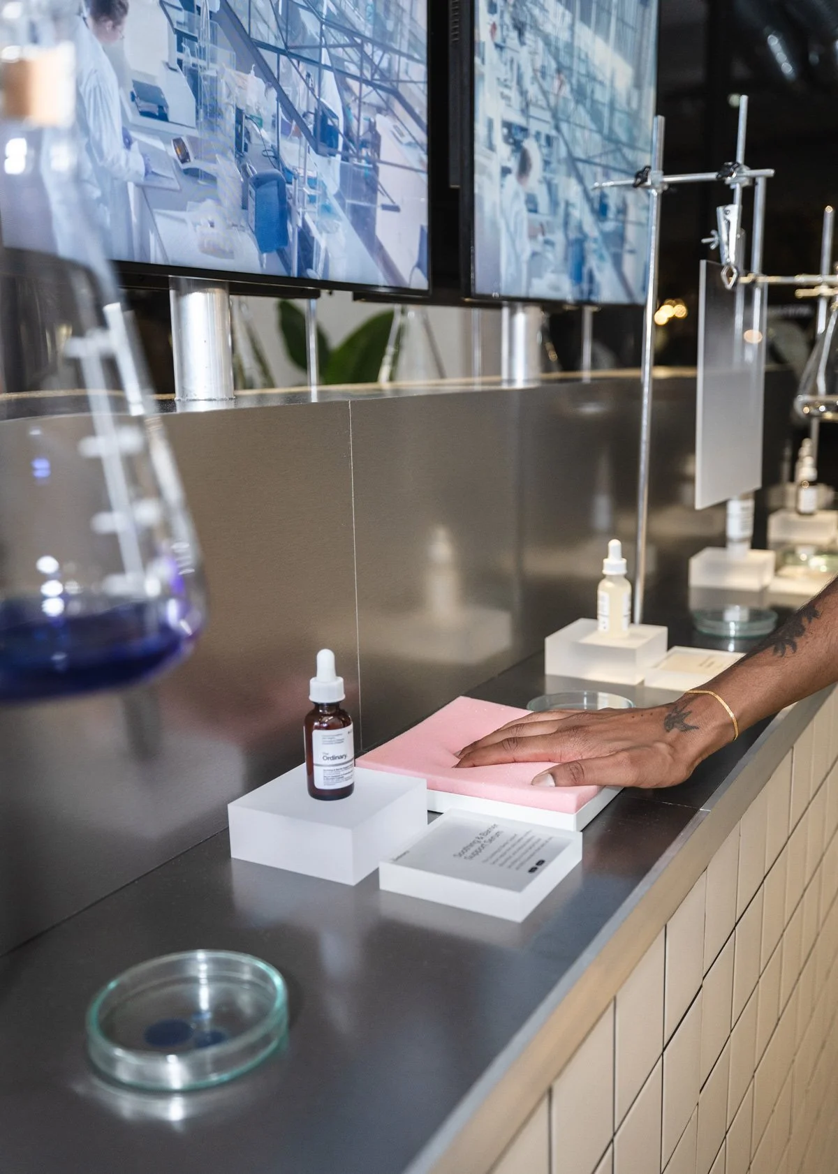 Interactive product presentation with laboratory props and suspended glassware on tiled display system, display design and props styling by Steffi Bühlmaier for The Ordinary x Highsnobiety temporary showroom, event production by PS:KAAS, photography 