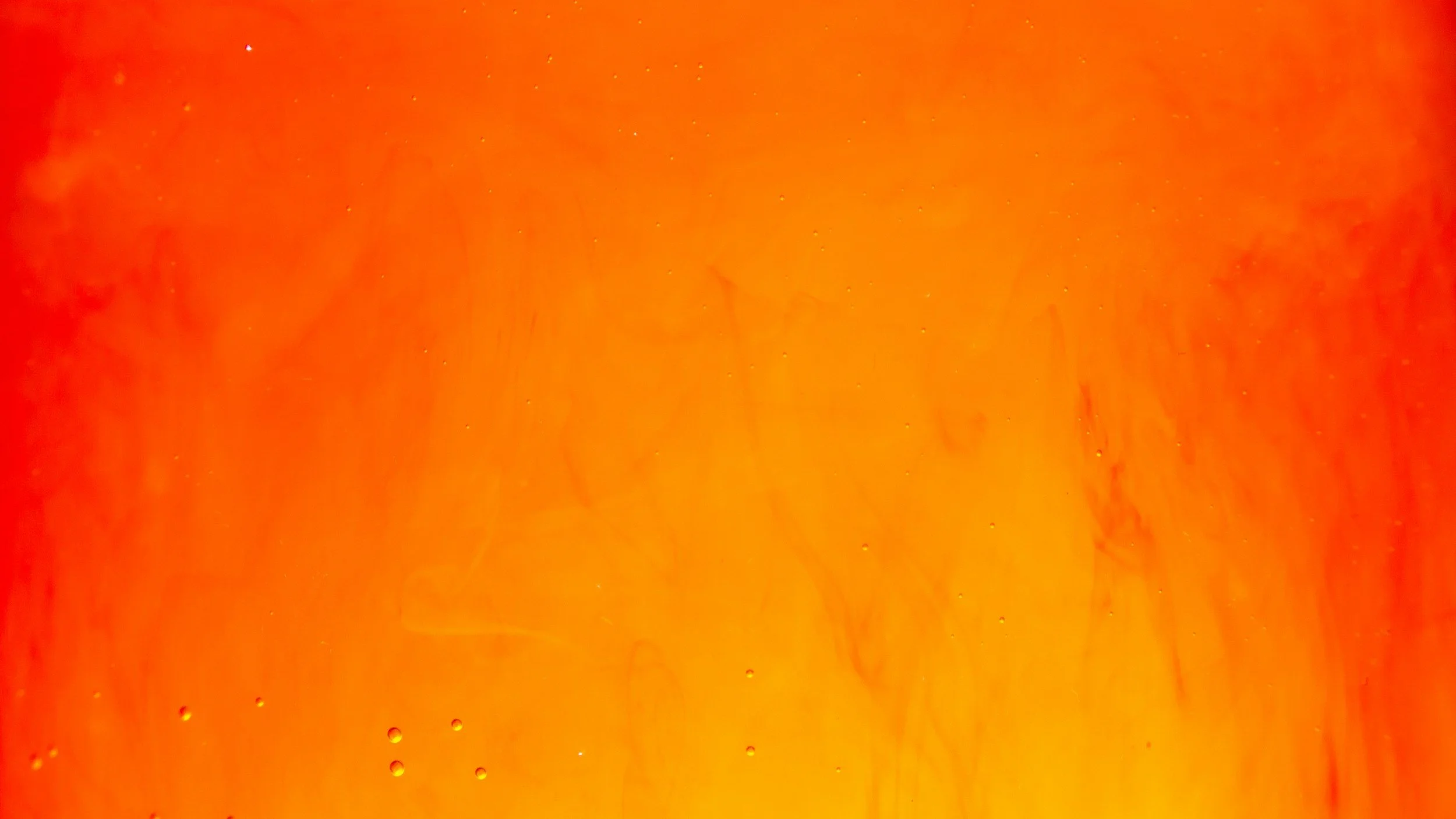 Close-up photograph of bright orange liquid with swirling patterns and small bubbles.