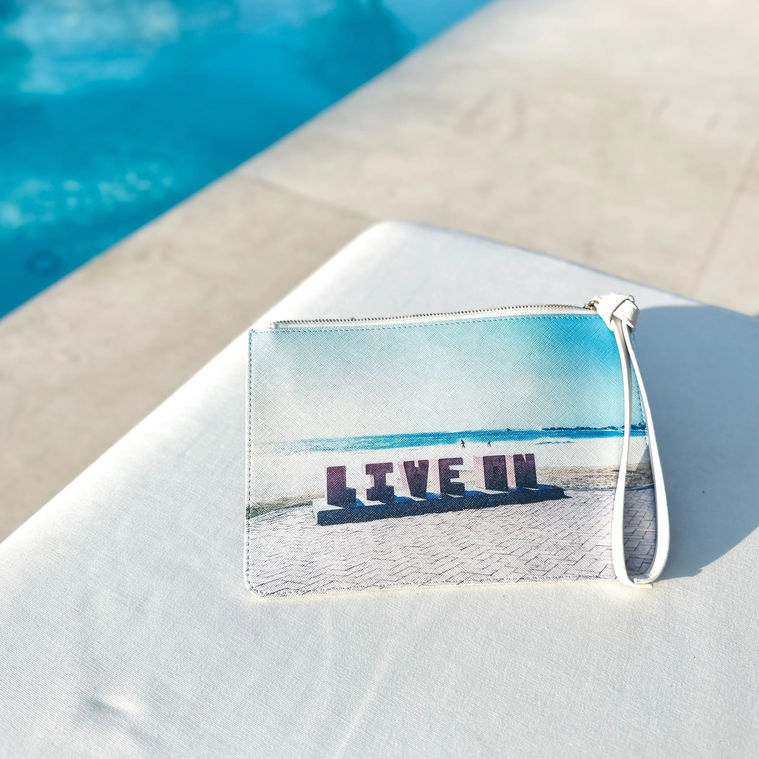 Design-Clutch mit original Fotoprint „LIVE IN“ von limiloulu. Stilvolles Accessoire für moderne Nomad:innen & kreative Reisende. Shot by the pool.