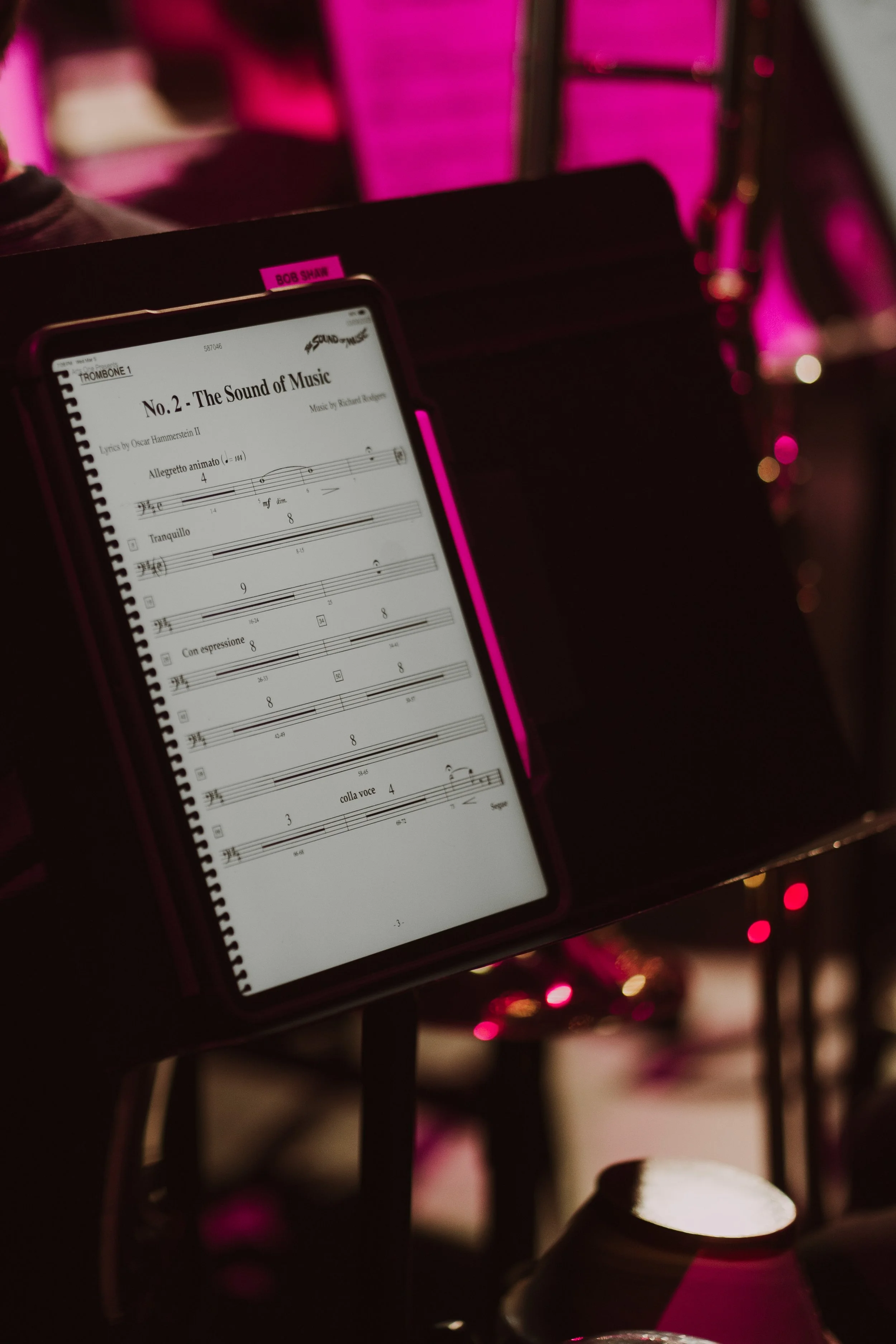 Digital sheet music displayed on a tablet screen for 'The Sound of Music,' with a black music stand and pink lighting in the background.