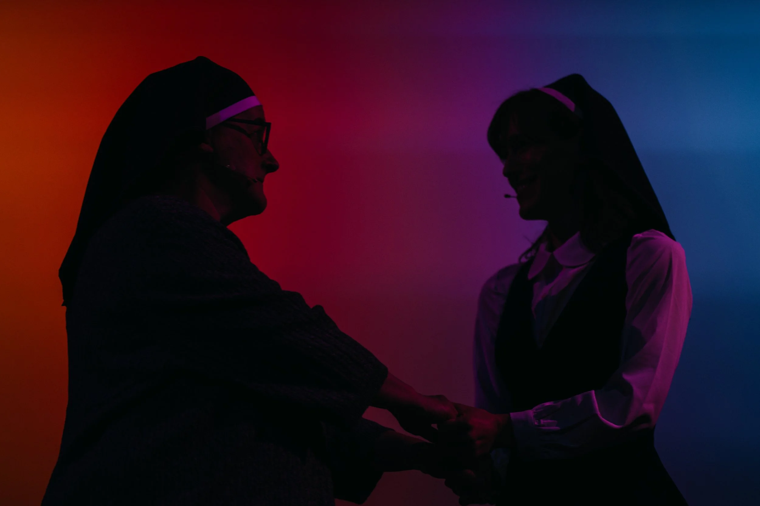 Silhouettes of two nuns holding hands and smiling against a multicolored background.