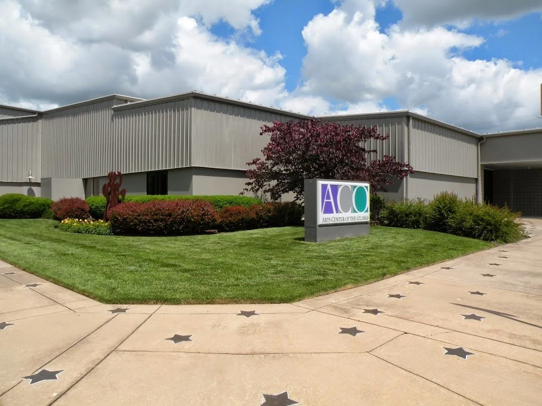Exterior view of the Arts Center of the Ozarks building with landscaped area, a sign reading 'Arts Center of the Ozarks,' and a cloudy sky.