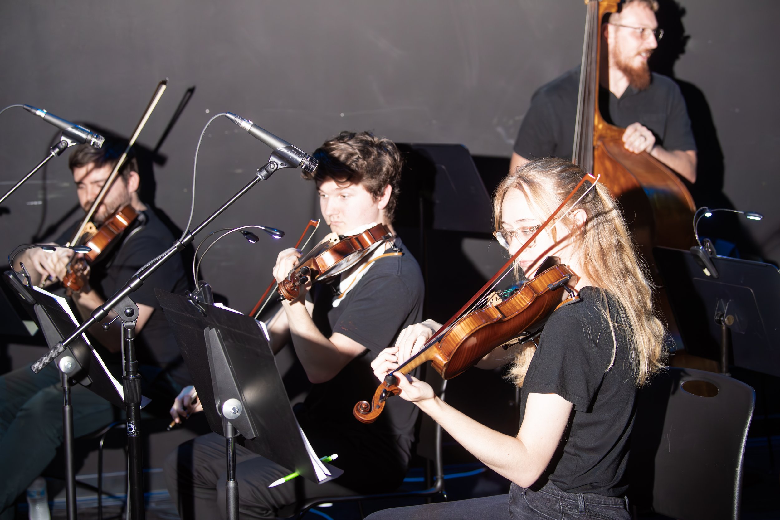 Young musicians playing violins and a double bass during a rehearsal or performance.