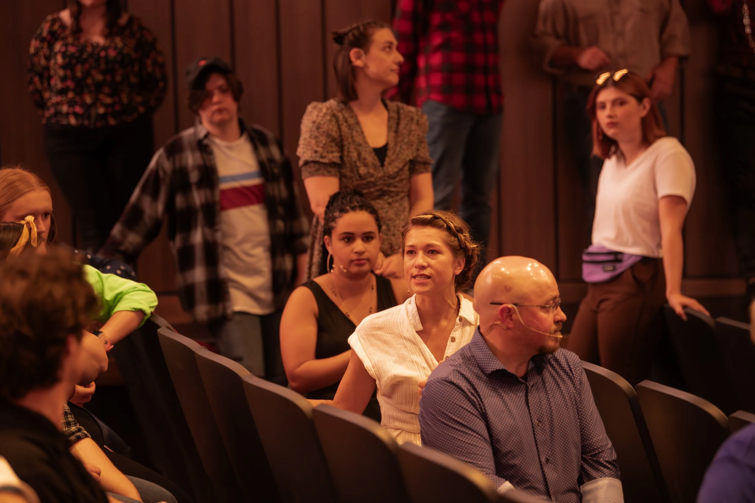 Audience members seated and standing in a theater or auditorium, engaged and listening to a performance or speaker.