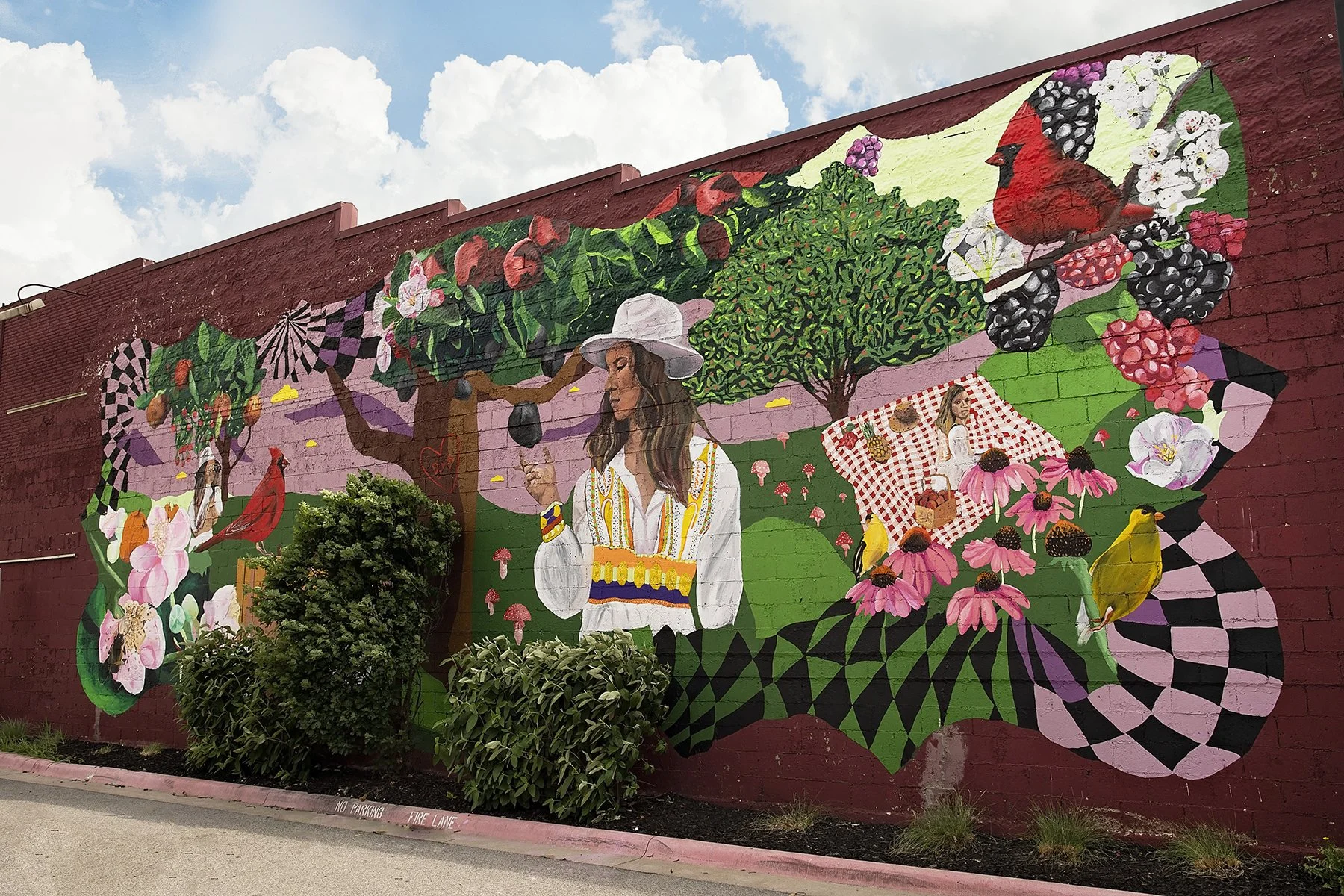 Colorful mural on a brick wall depicting a woman among trees, flowers, and birds, with pink, green, purple, and black patterns and details.