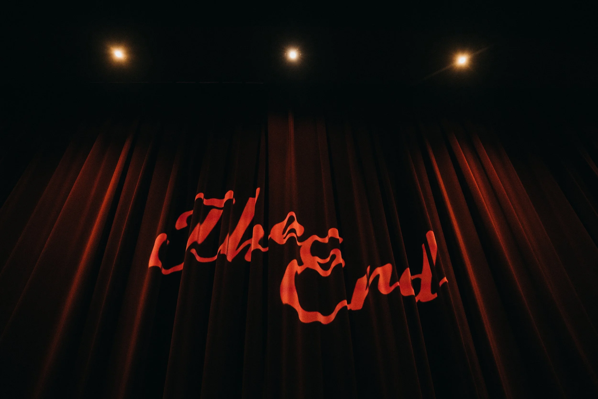 Red neon sign reading 'Caution' behind dark curtains in a dimly lit room.