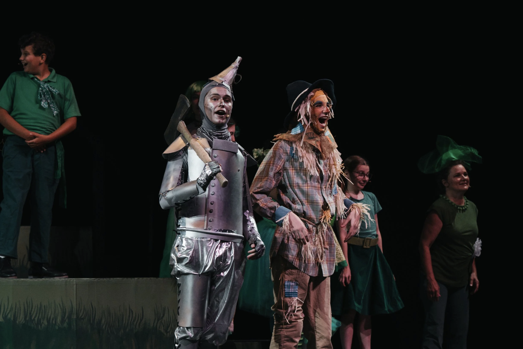 Children and adults performing in a theatrical play, dressed in costumes inspired by fairy tales and fantasy characters, on a stage with a dark background.