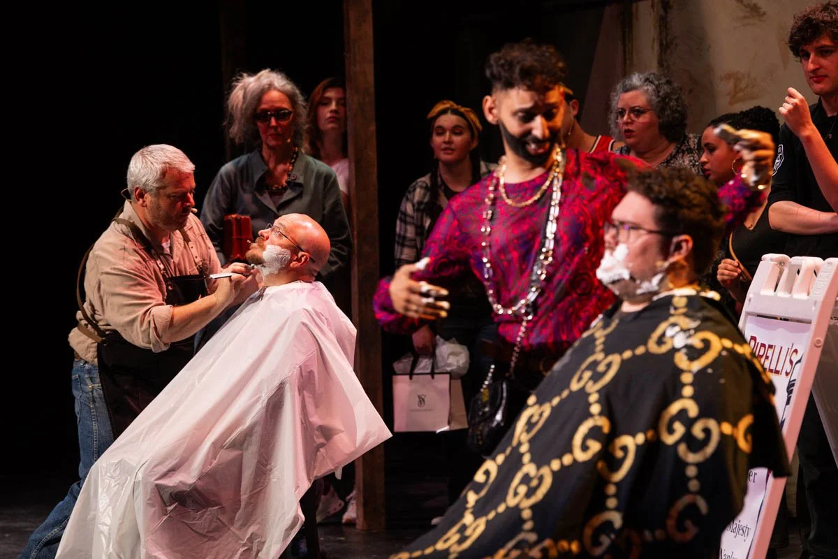 Actors performing a comedic scene in a play, with some characters having fake shaving cream on their faces, set in a vintage barber shop or salon setting.