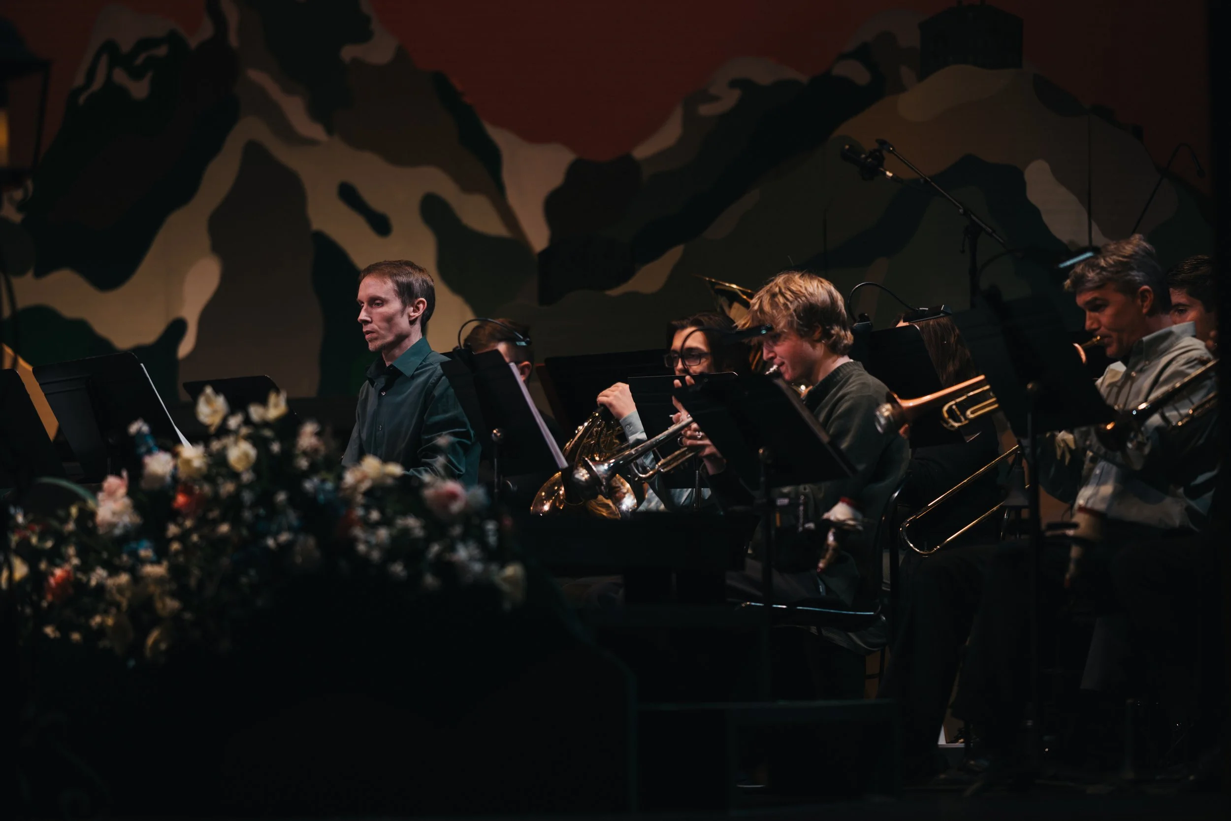 Group of musicians performing on stage, with a backdrop of mountains painted on the wall.