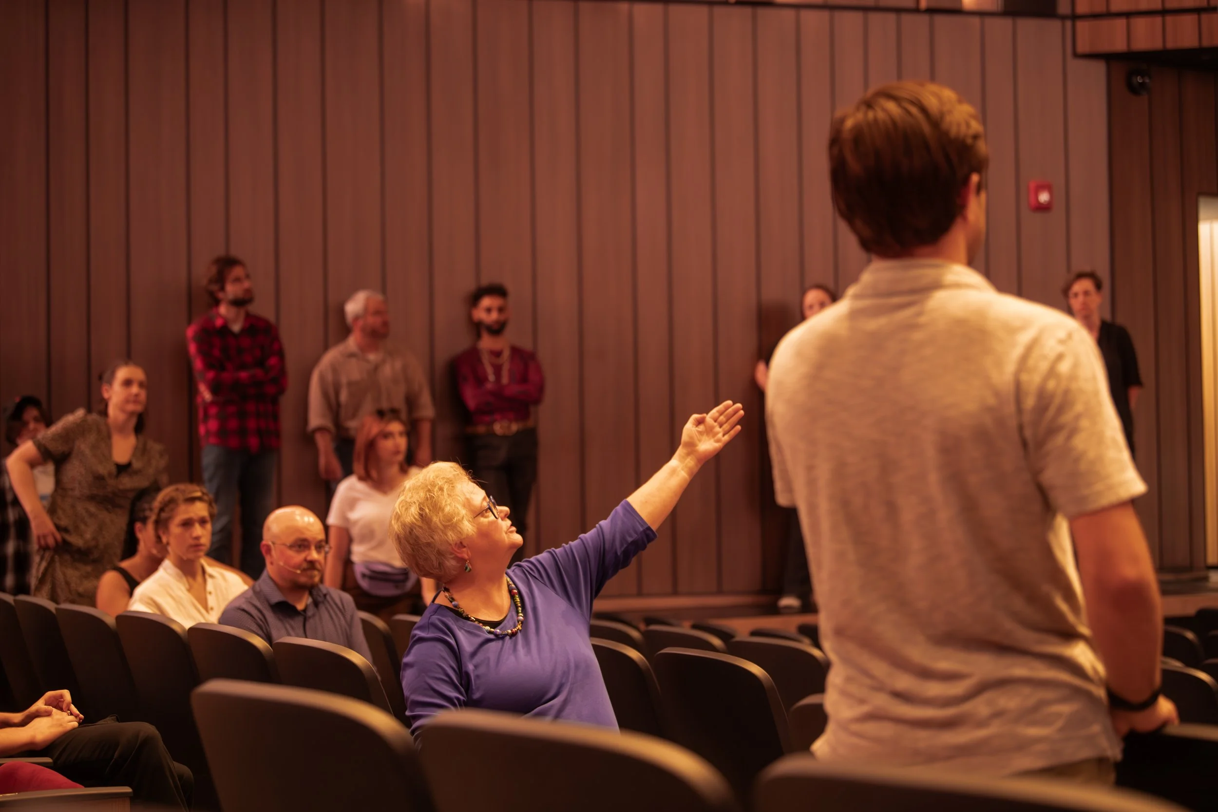 Woman raising her hand in a discussion in a conference room with seated and standing audience members.
