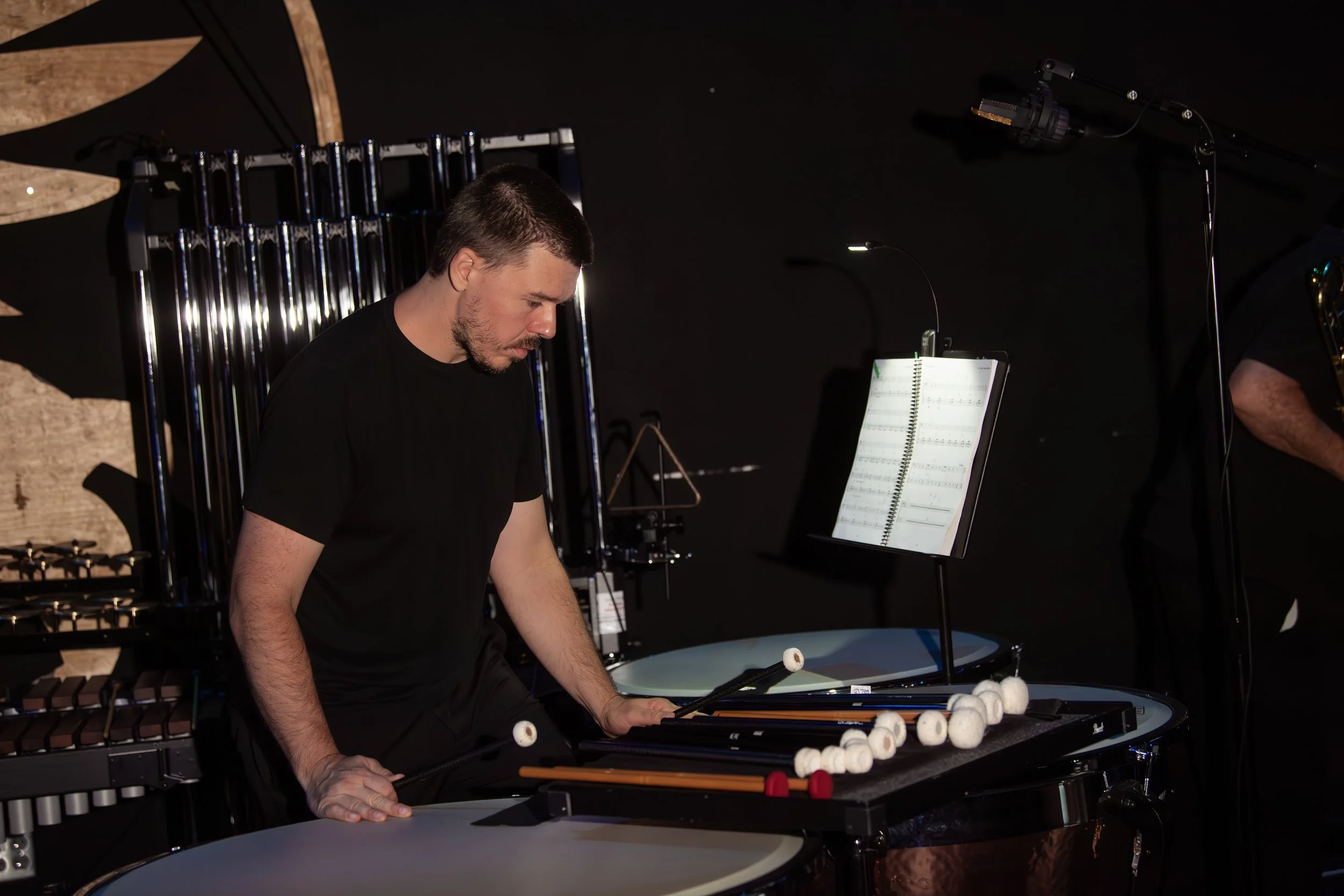 A musician playing percussion instruments in a dark room with sheet music on a stand.