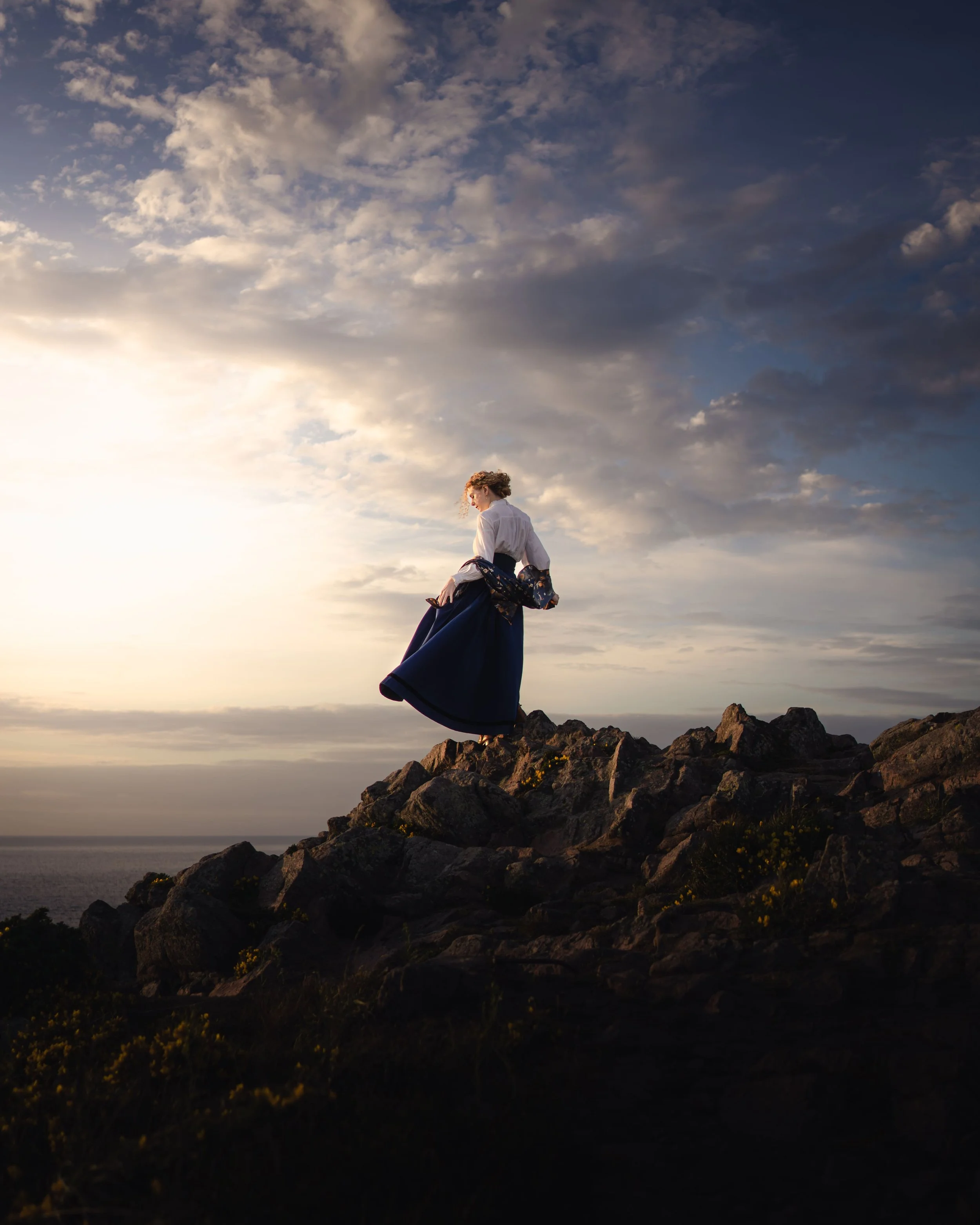 Portrait d'une femme en vêtements victoriens au bord d'une falaise en Bretagne dans une ambiance coucher de soleil