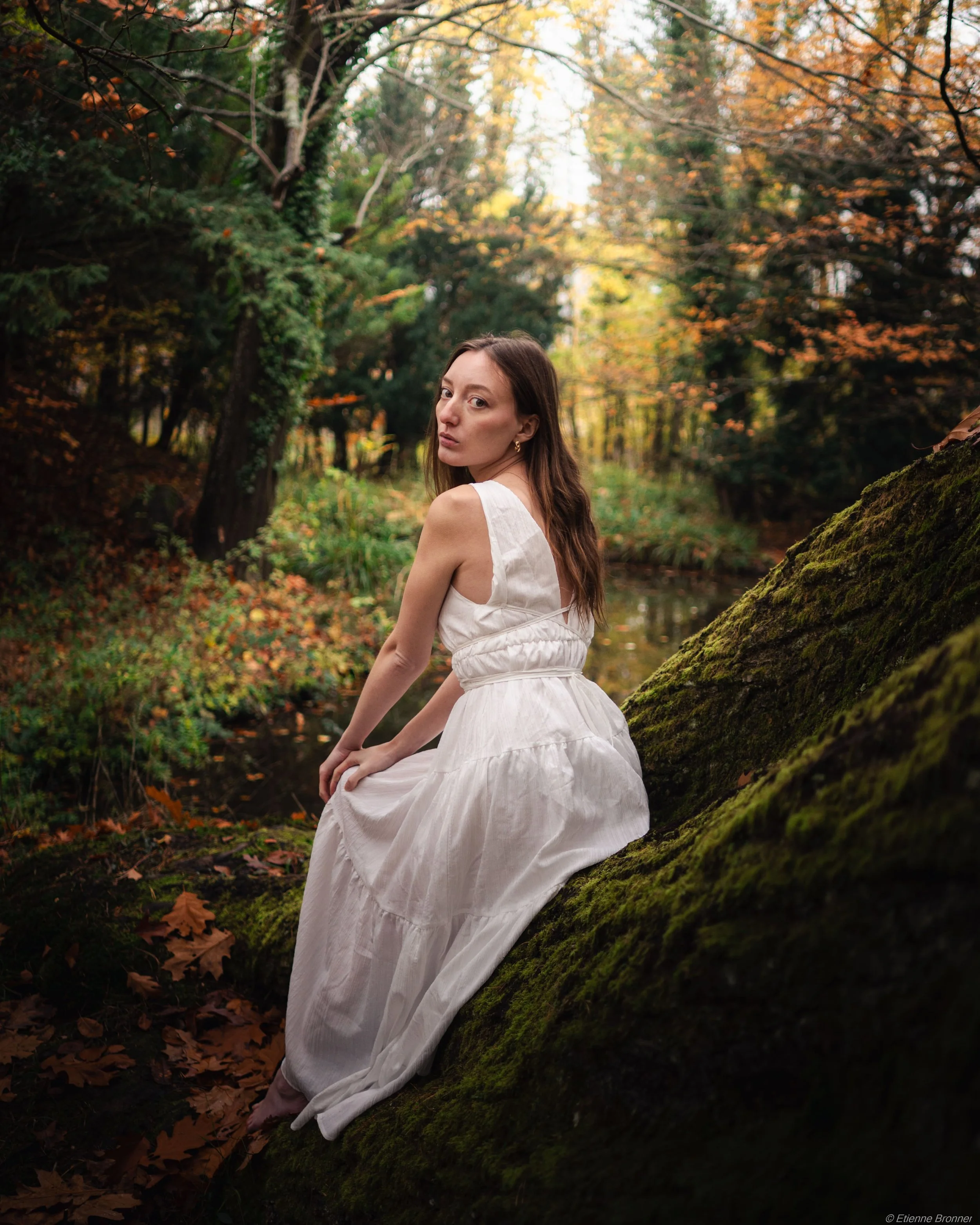 Portrait d'une femme assise sur un tronc au bord de l'eau en automne au domaine du Windeck