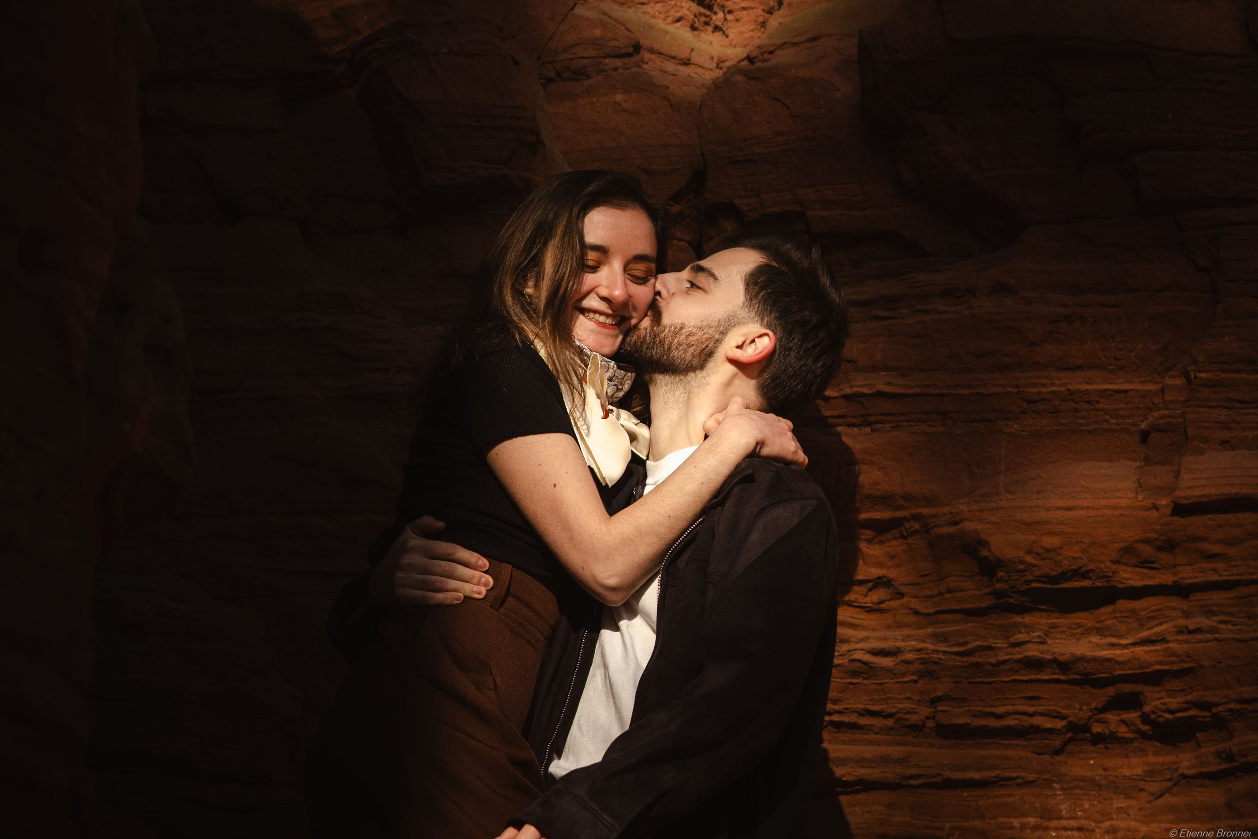 Un couple embrassant et souriant dans un décor rocheux, ambiance chaleureuse et intime.