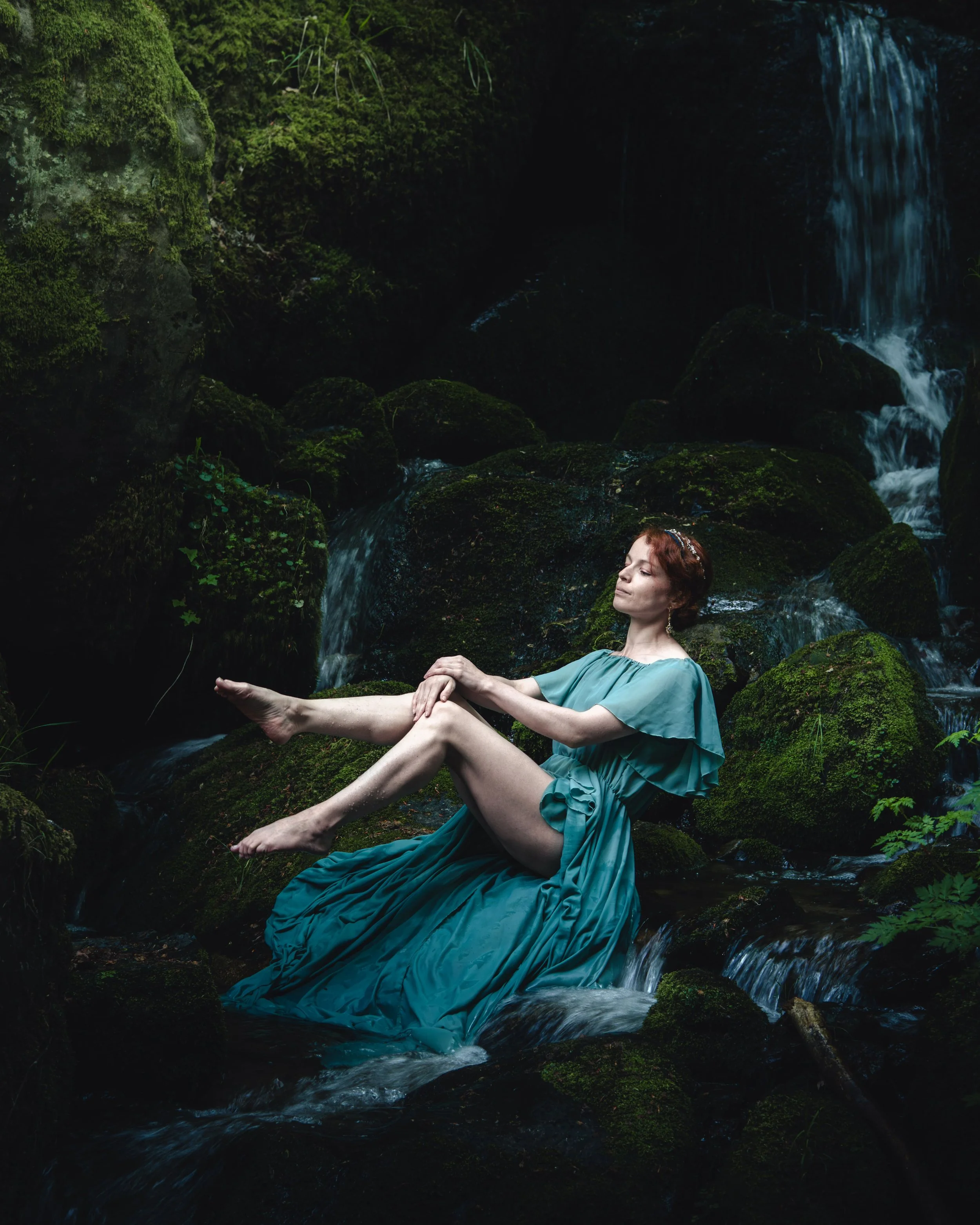 Portrait d'une femme aux cheveux roux dans une robe bleu-vert, assise sur des rochers au bord d'une rivière proche de la cascade du Hohwald en Alsace.