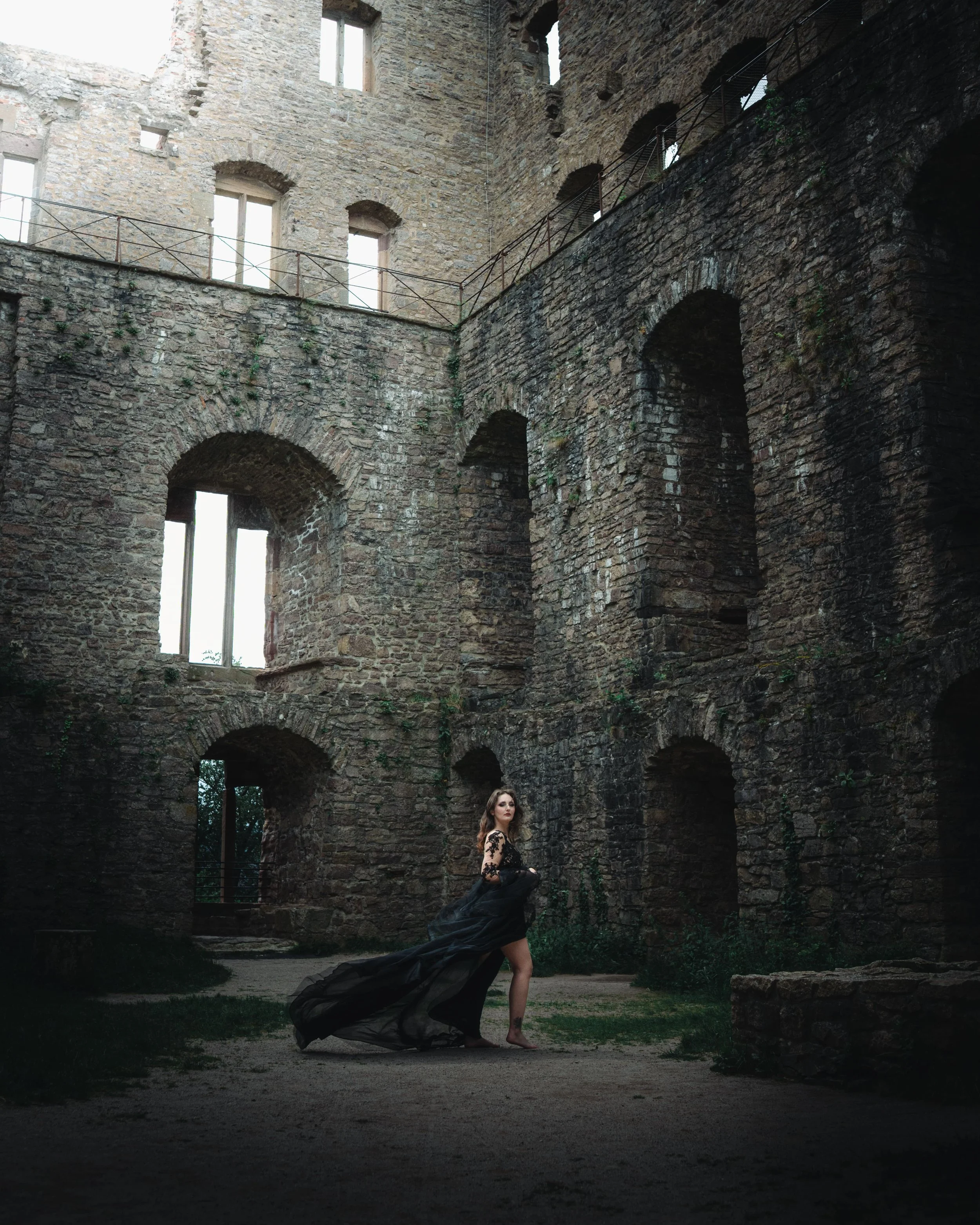 Portrait d'une femme portant une robe noire longue et transparente posant dans une ruine ancienne en pierre, avec un ciel nuageux en arrière-plan, au château de Hohenbaden.