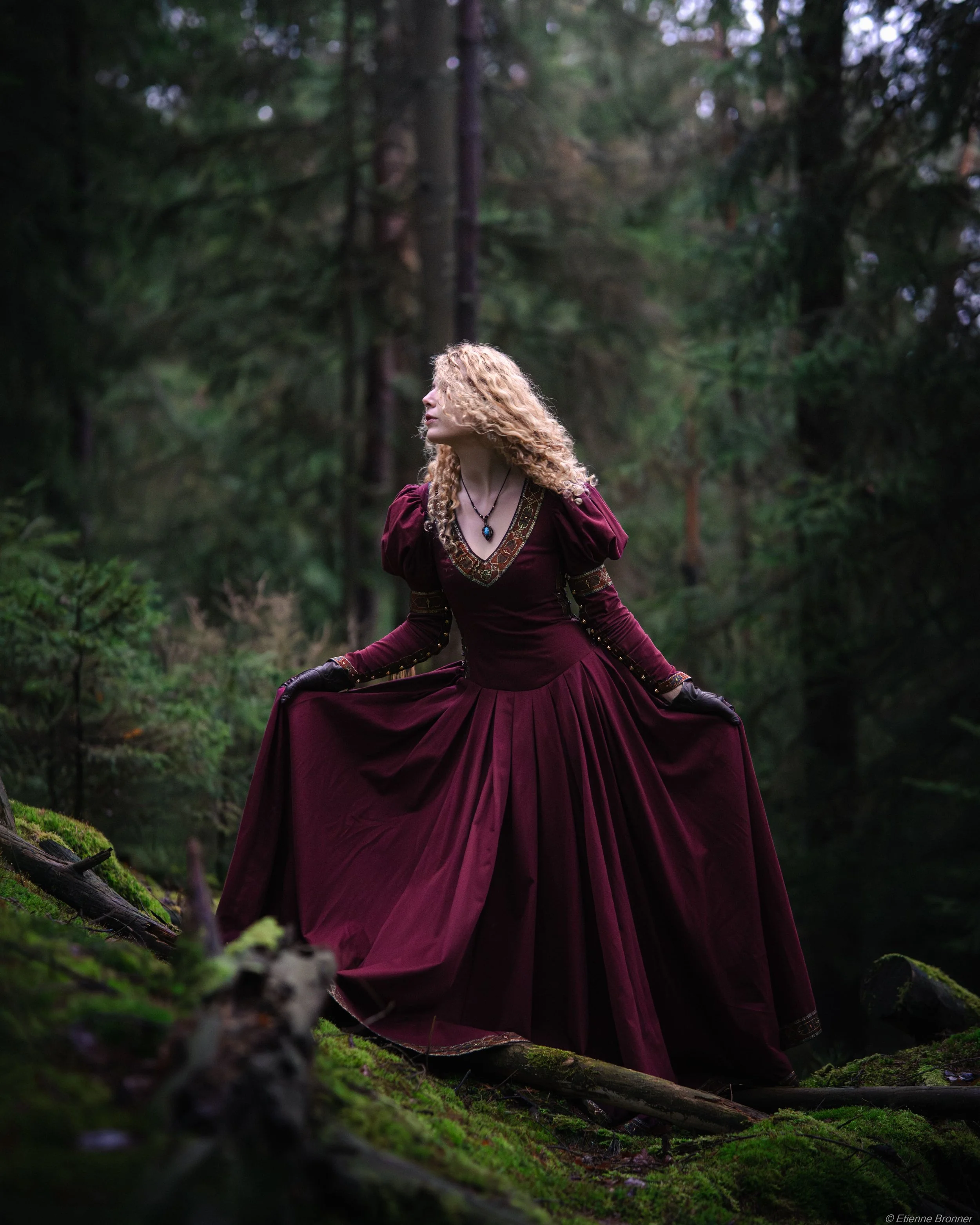 Une femme en robe longue bordeaux dans une forêt verte.