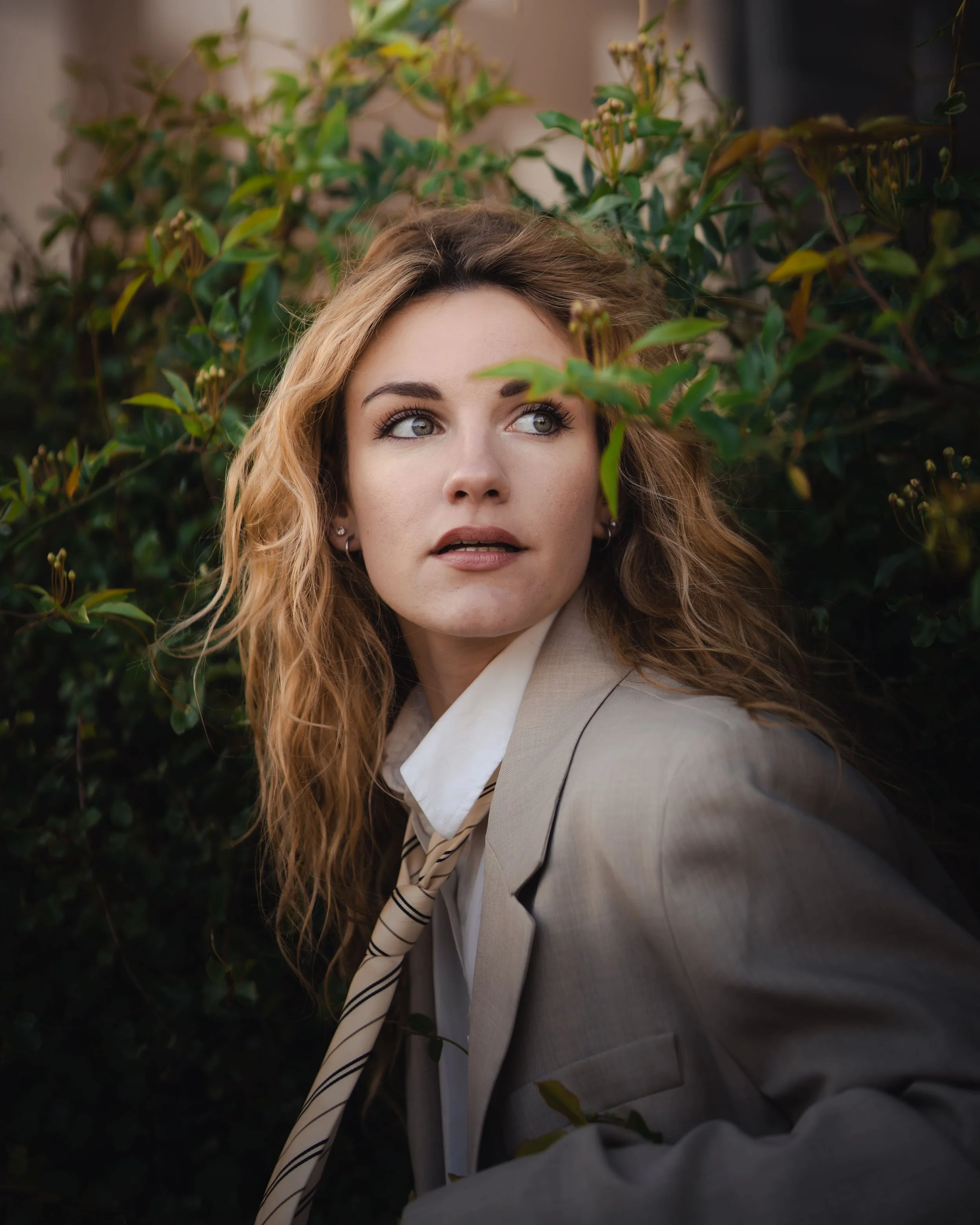 Portrait d'une femme aux cheveux bouclés assise dans un environnement naturel entourée de feuillage vert, à l'hôtel de ville de Montpellier.