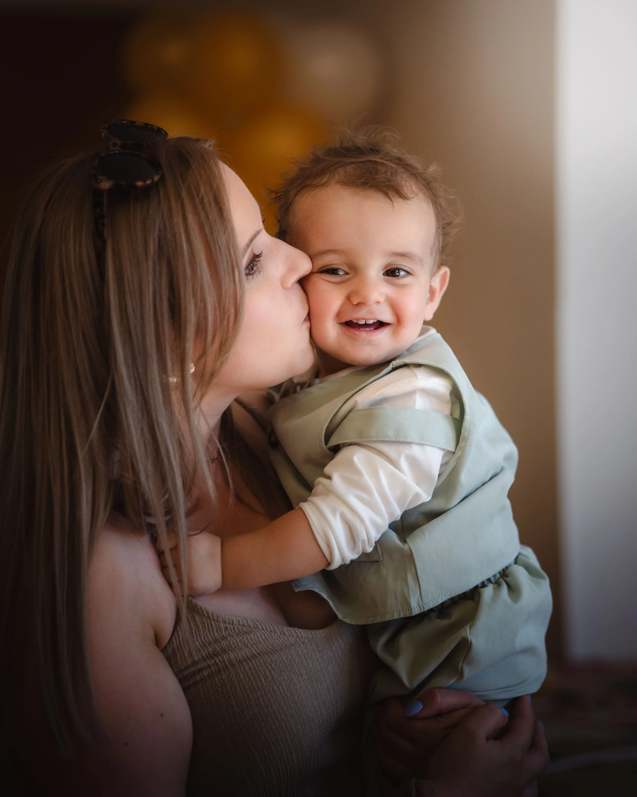Portrait d'une femme embrasse un jeune enfant qui sourit, avec un arrière-plan flou et des lumières douces, lors d'un mariage en Alsace.