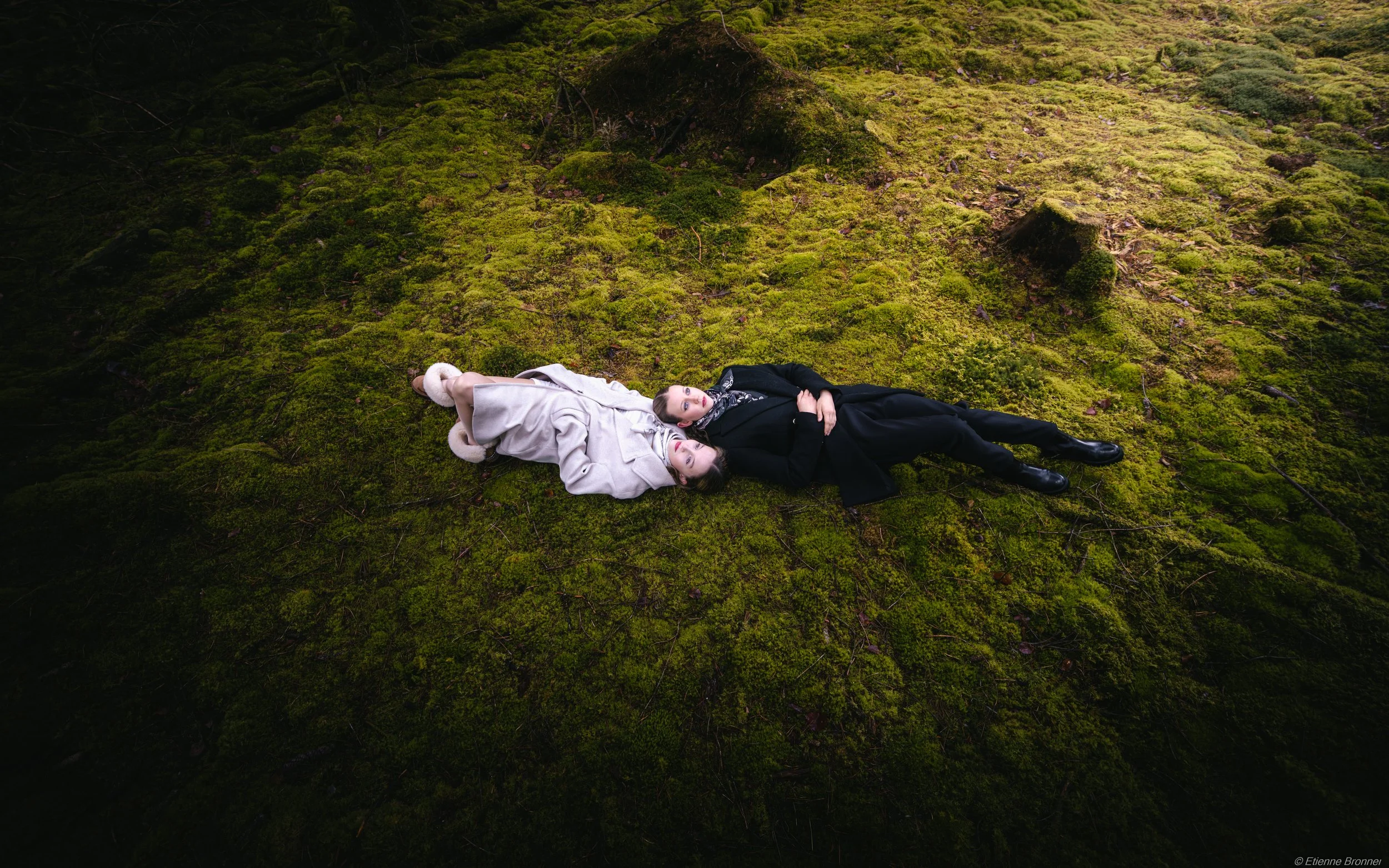 Portrait de deux femmes allongées sur un tapis de mousse verte dans une forêt vosgienne.