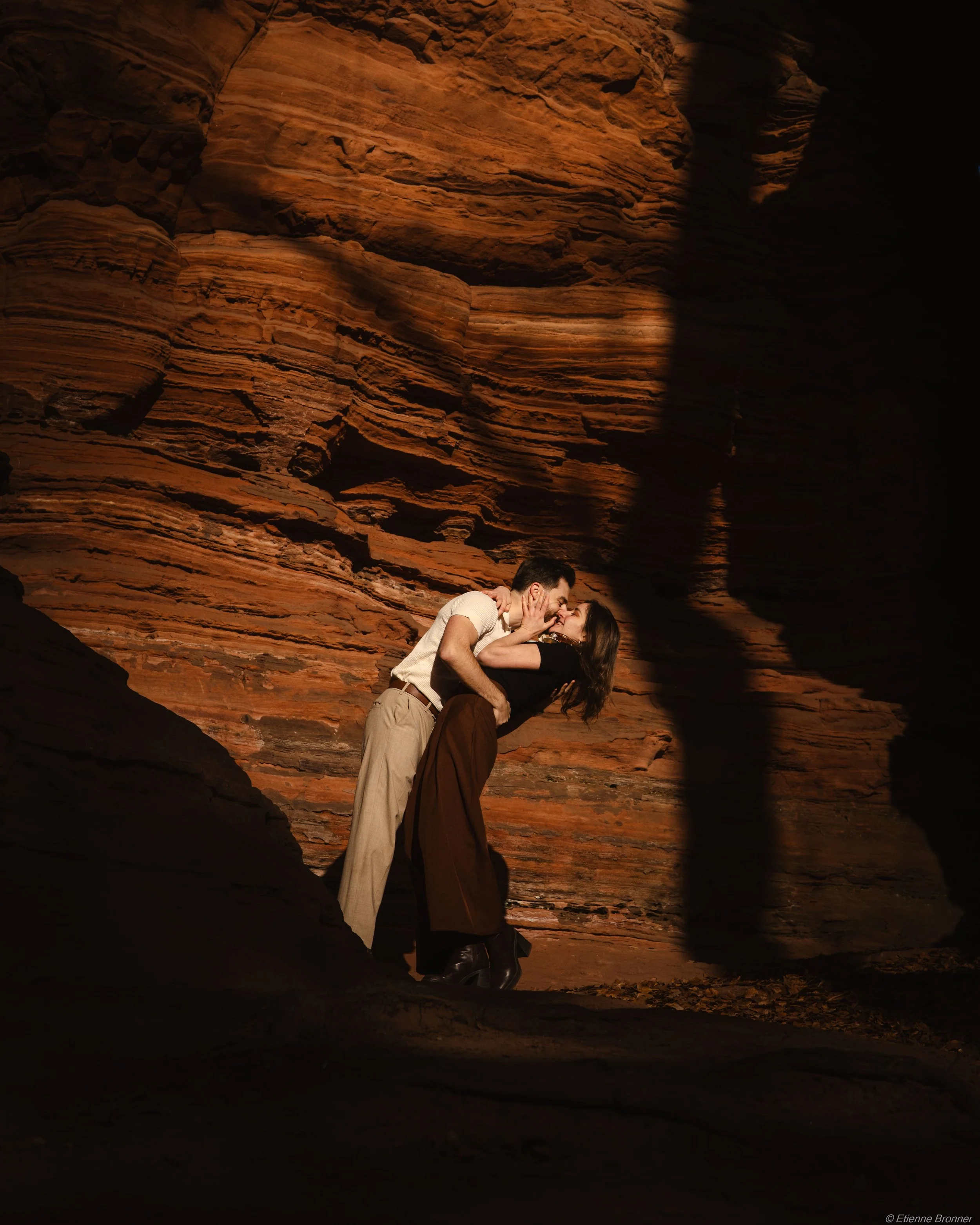 Un couple s'embrasse dans un canyon rocheux avec des ombres accentuées par la lumière du soleil.