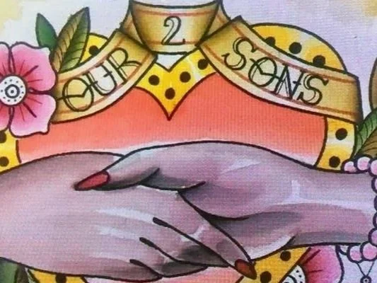 Tattoo of two hands clasped in front of a heart with flowers and a banner reading 'Our 2 Sons'