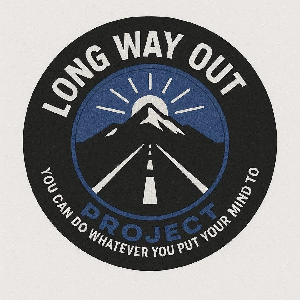 A circular sign with mountain and road illustration, the sun above the mountain, and text that reads, 'Long Way Out Project' and 'You can do whatever you put your mind to'.