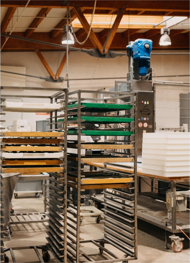 Metallregale mit grünen, braunen und weißen Backblechen in einer Industriewerkstatt