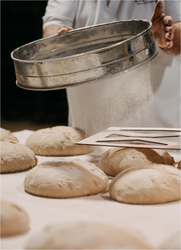 Backen von Brötchen, Mehl wird gesiebt, Hand in weißen Kleidungsstücken.