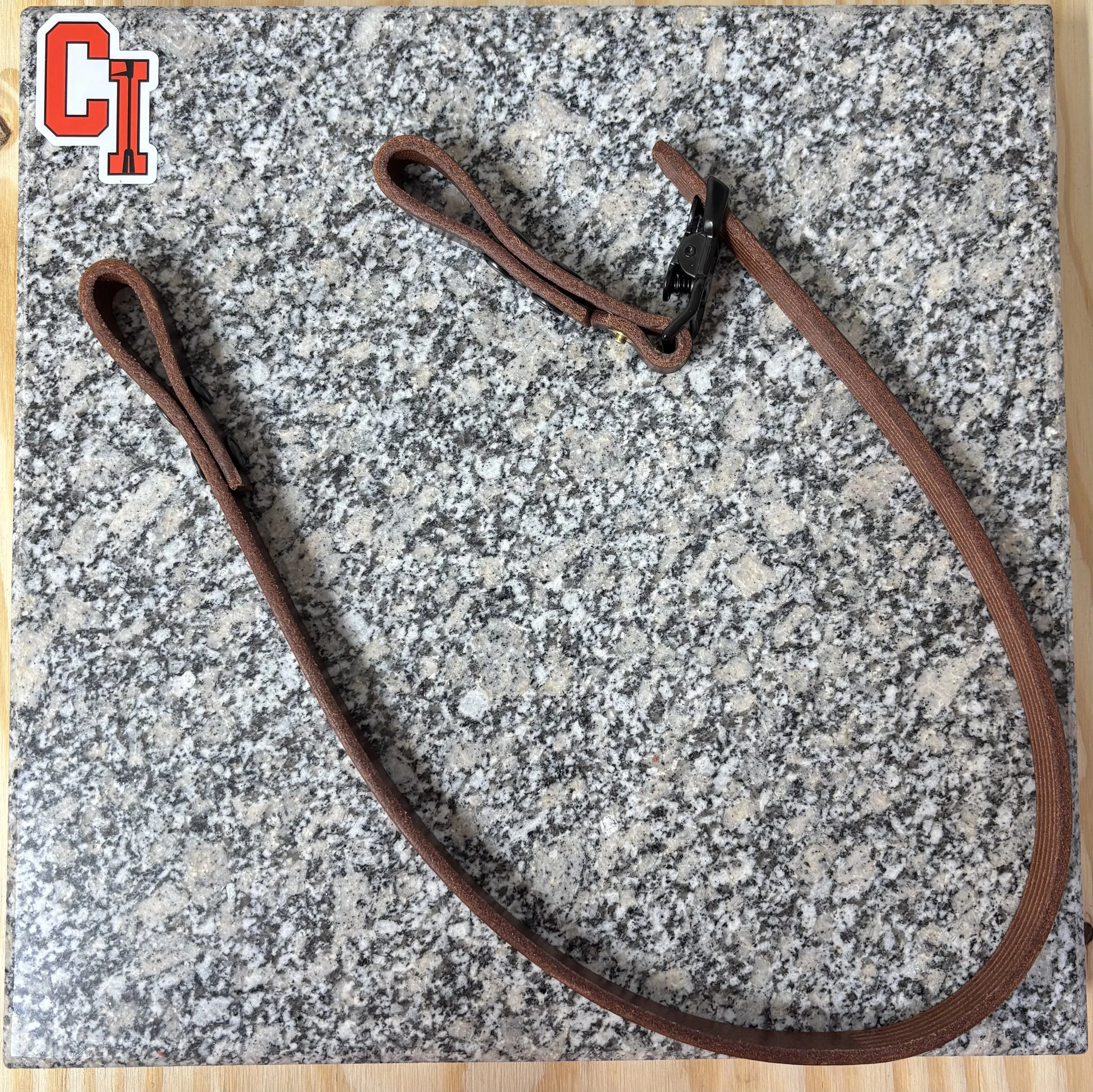Brown leather eyeglass or sunglasses strap with a black clip on a gray and white speckled surface.