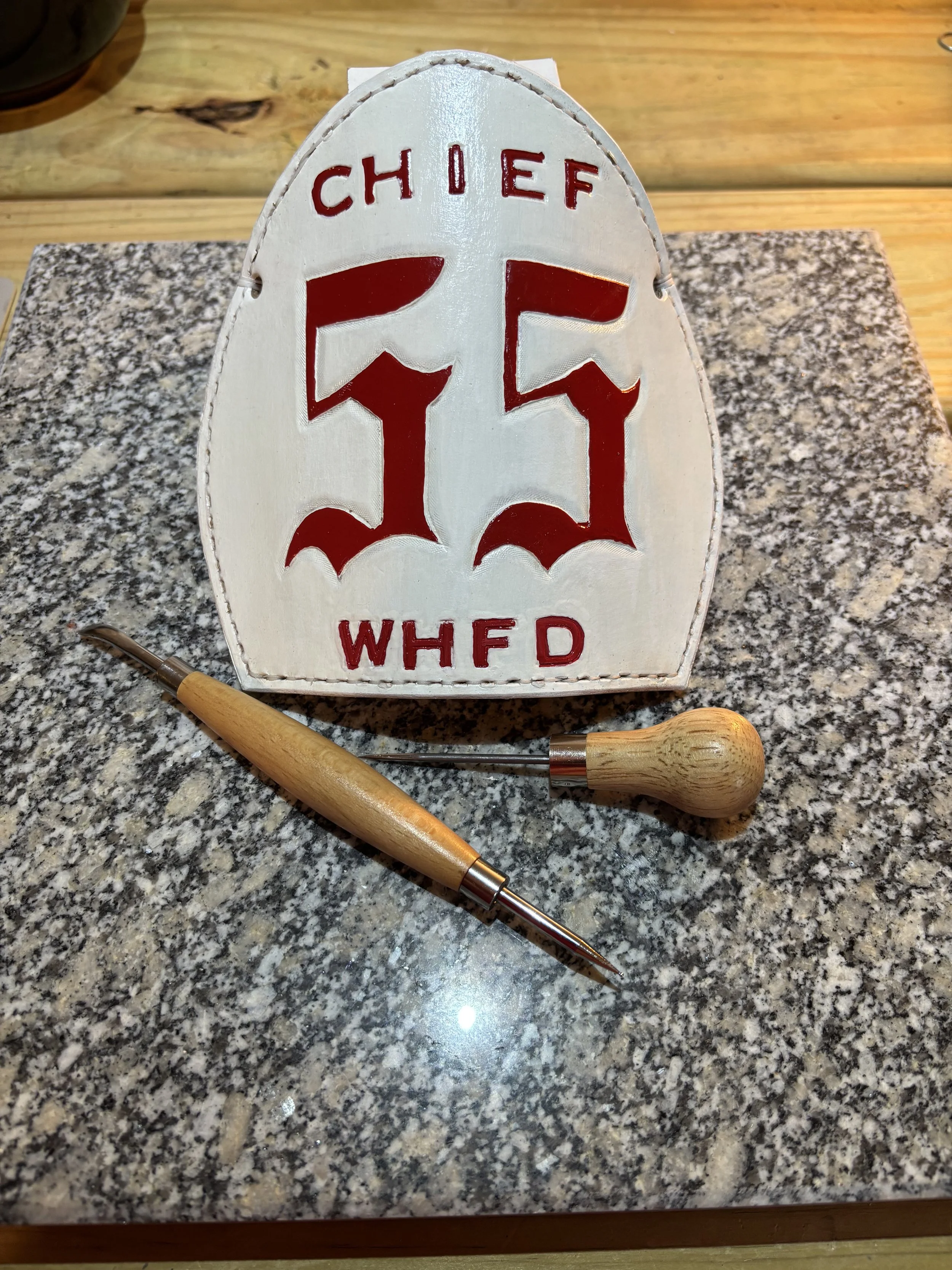 A vintage ceramic sign with the text 'Chief 15 WHFD' and a red number 15, placed on a granite countertop with a wooden-handled branding tool laid next to it.