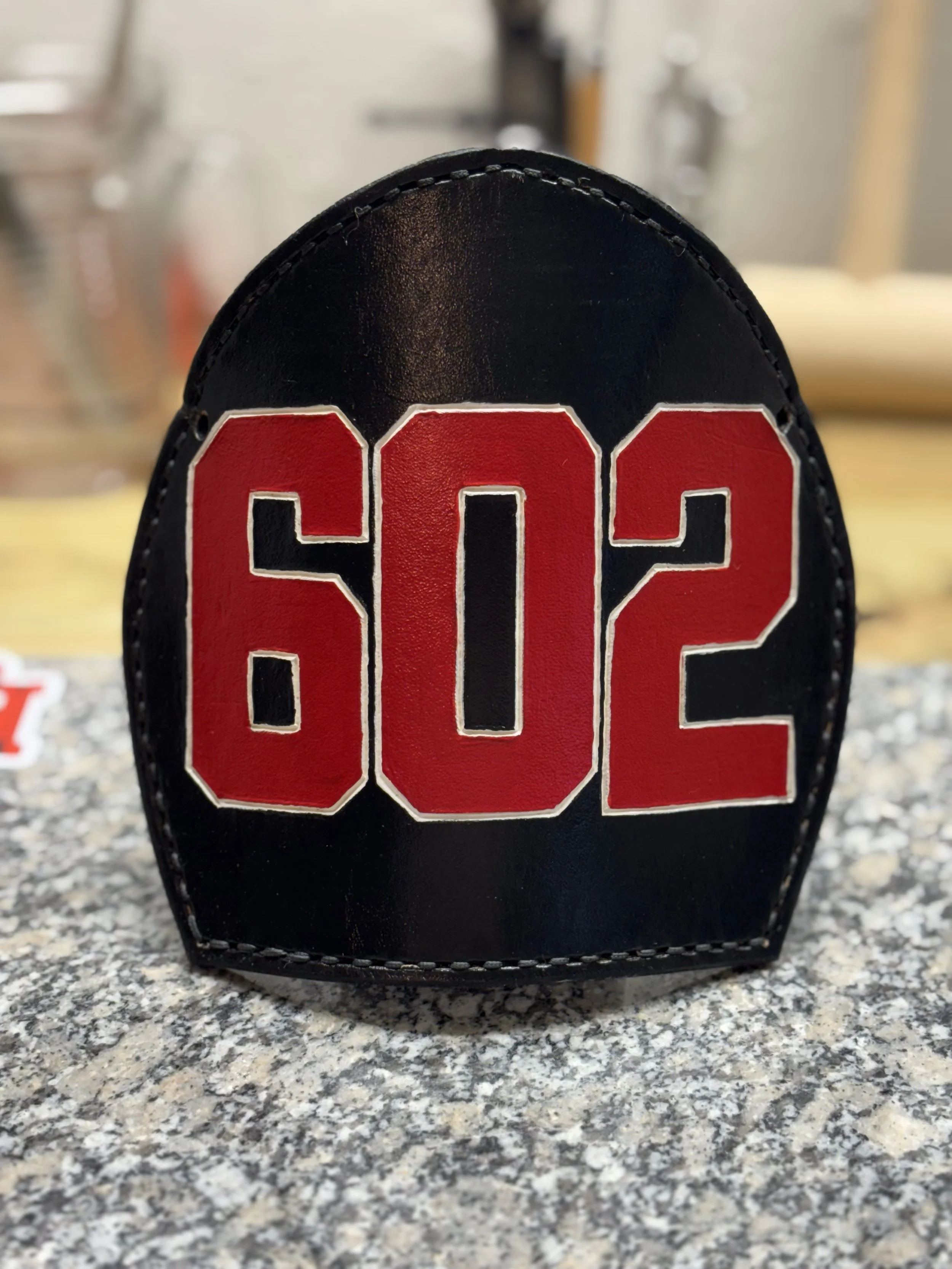A black leather patch with red and white embroidered text reading '.502' on a speckled gray surface.