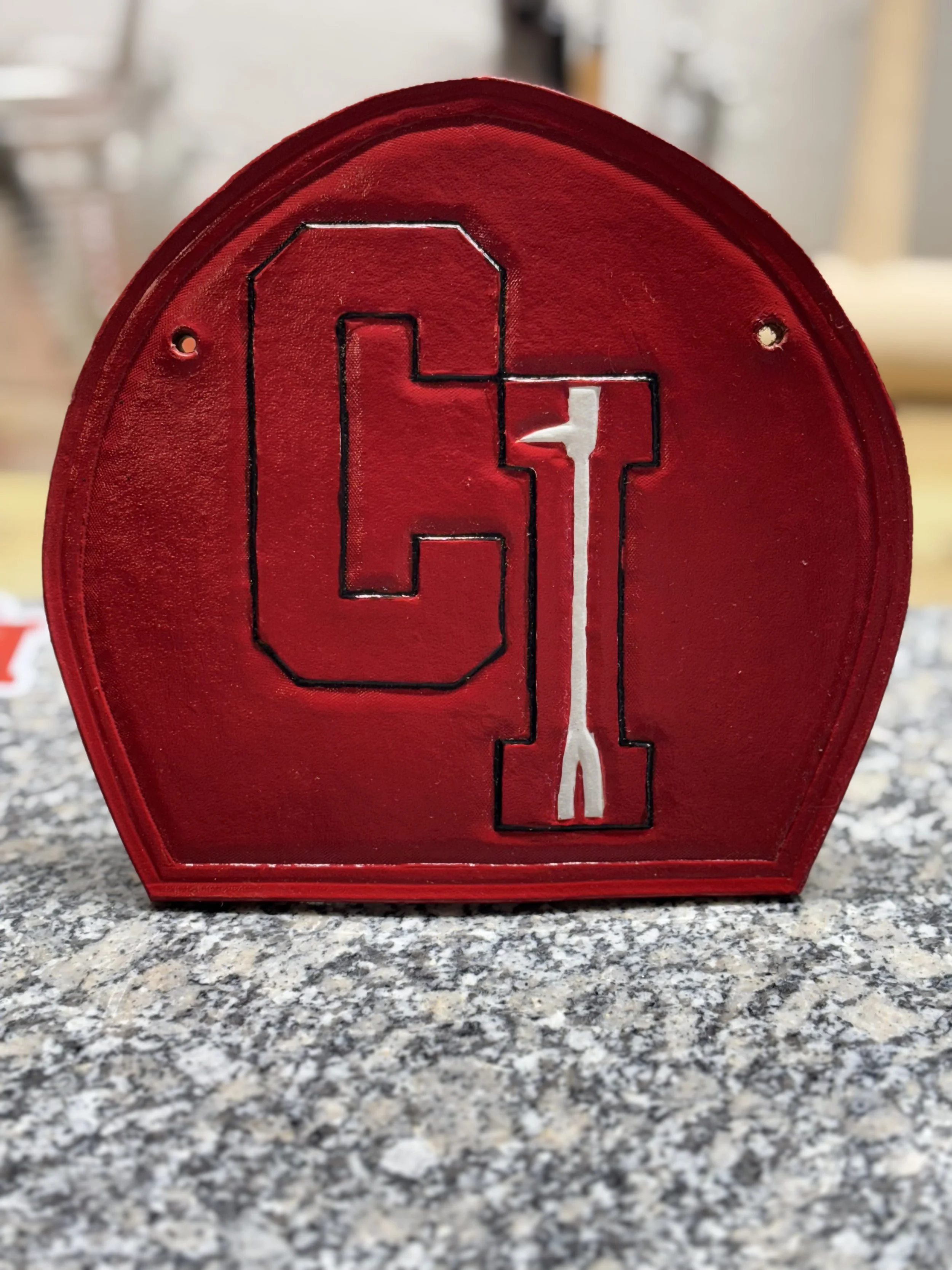 A red object with black outline of a large letter 'O' and a white outline of a large letter 'I' inside it, placed on a gray granite surface.