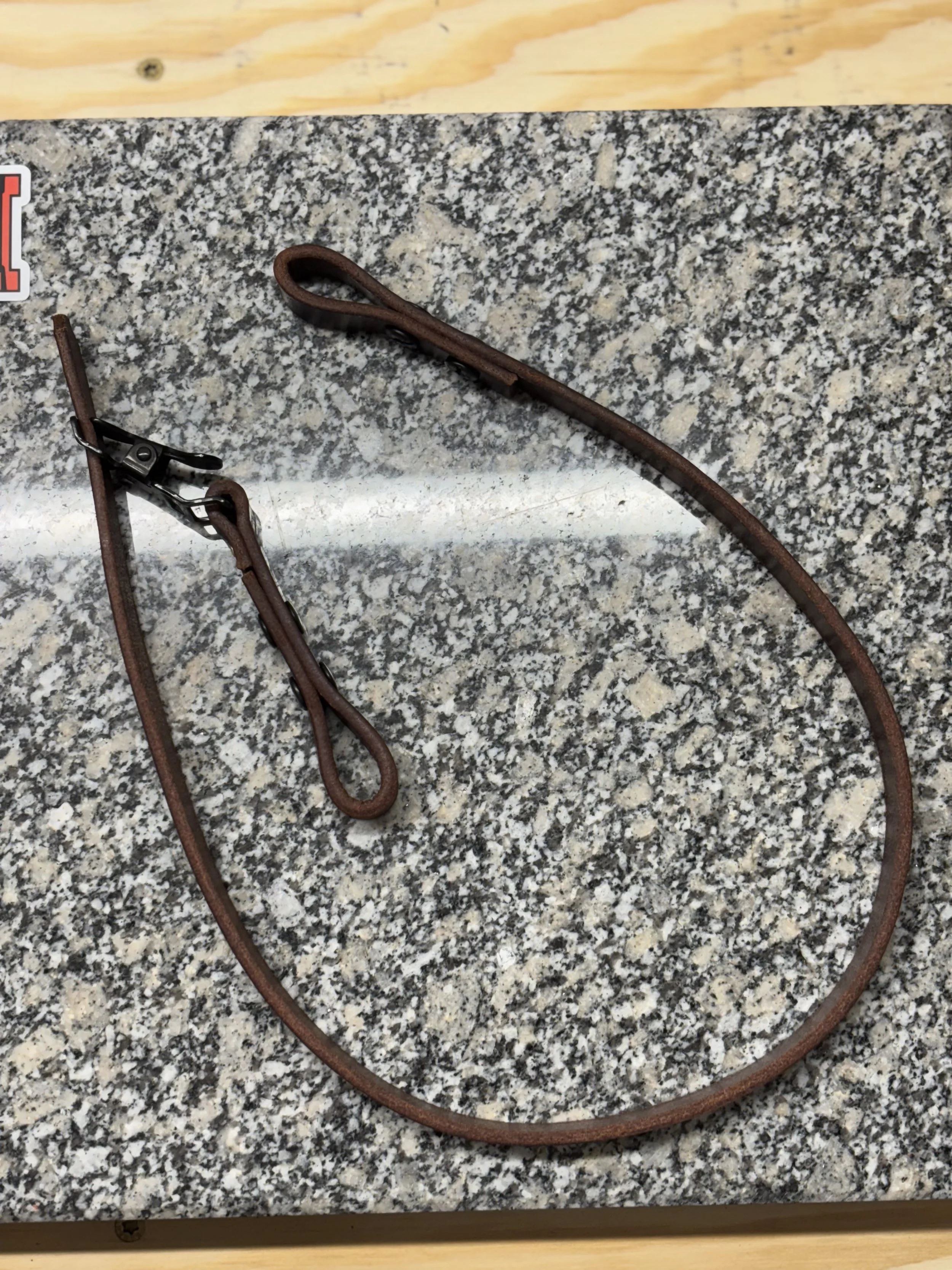 A brown leather strap with metal hardware laying on a speckled gray granite surface.