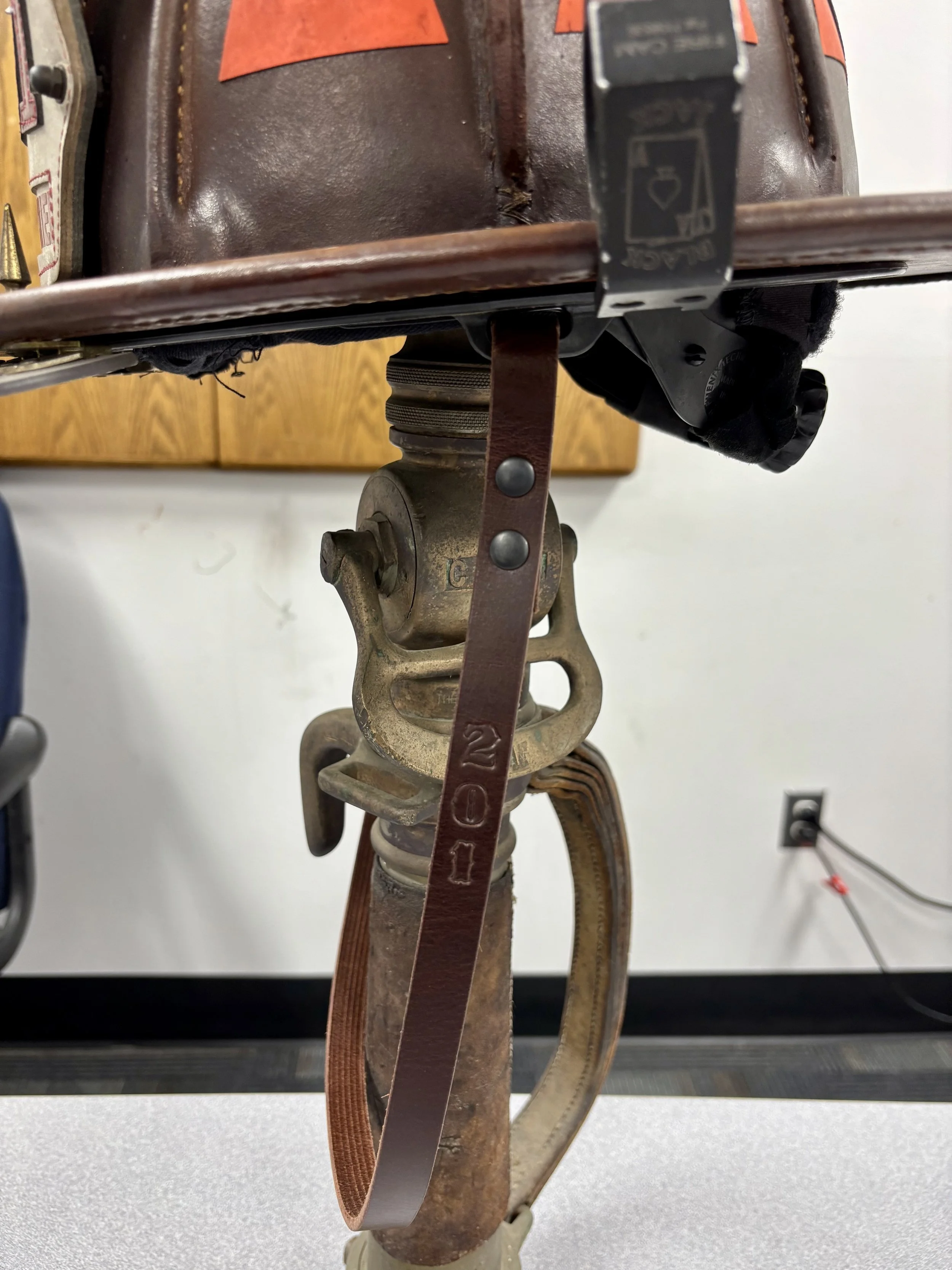 Close-up of an old baseball catcher's mitt attached to a vintage metal leg brace with a leather strap, on a white table in a room with cabinets and wall outlet in the background.