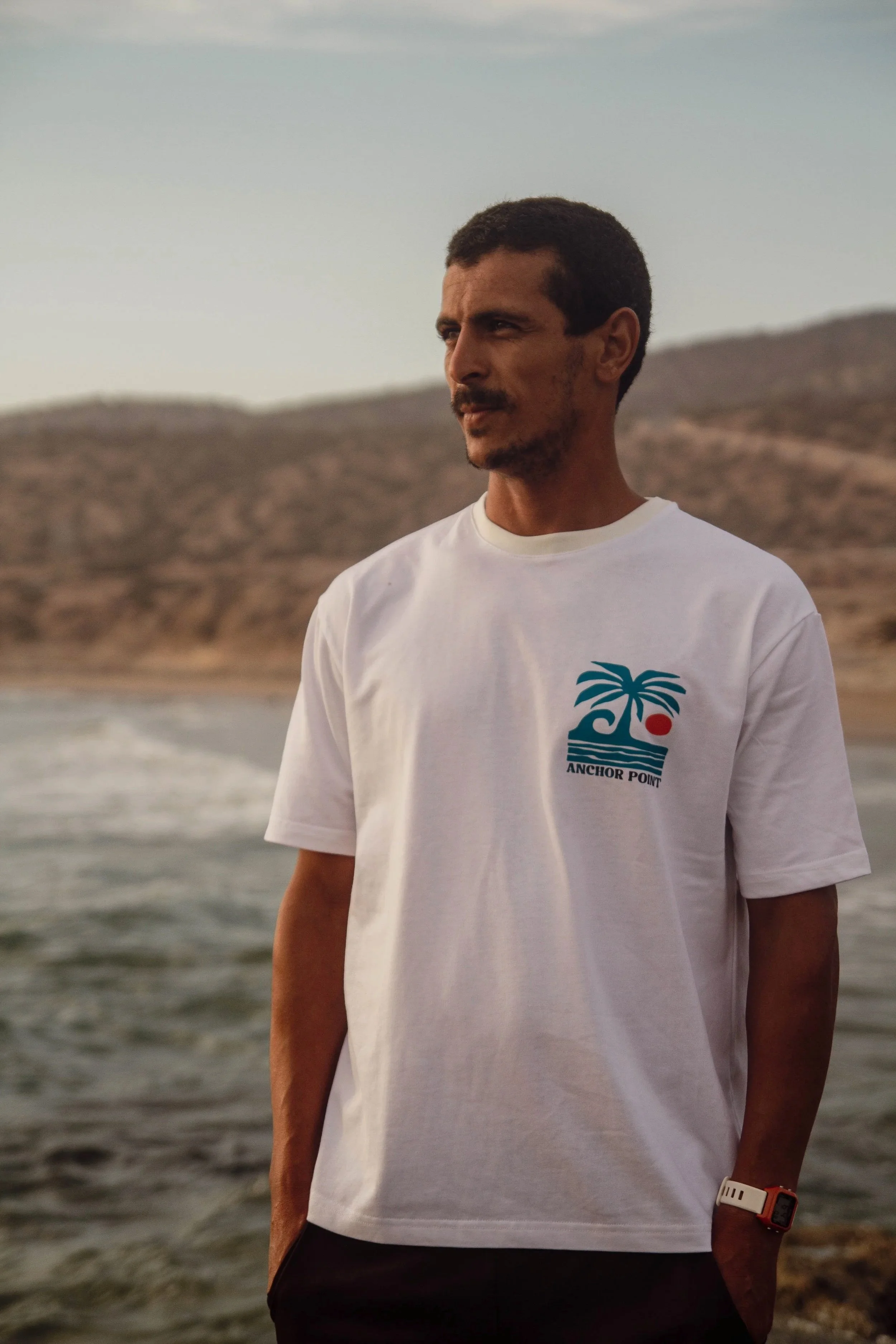 White Anchor Point T-shirt, standing on the rocks at Anchor Point, Taghazout in Morocco.