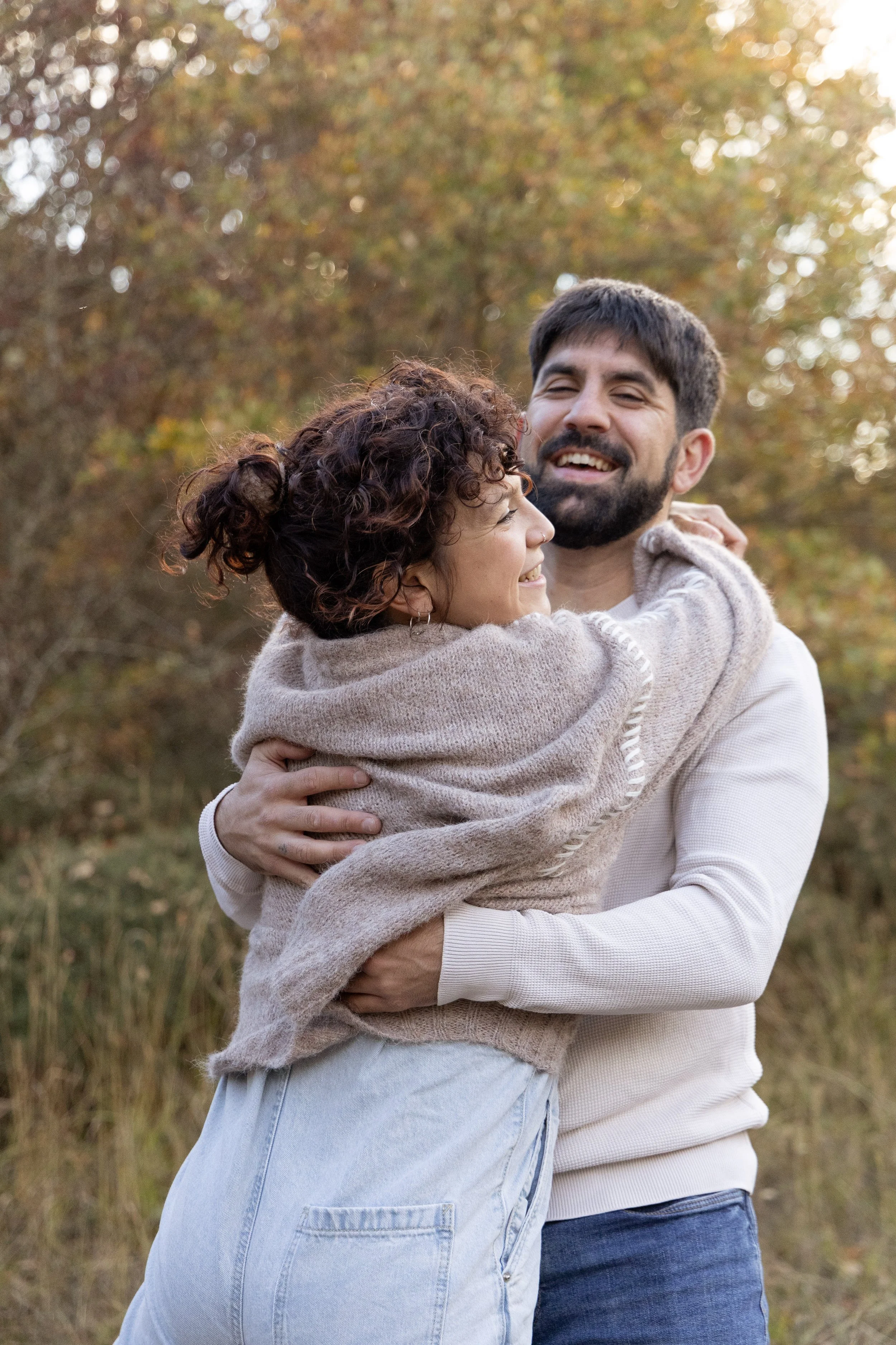 A man and woman hugging outdoors in a park during autumn, smiling at each other.