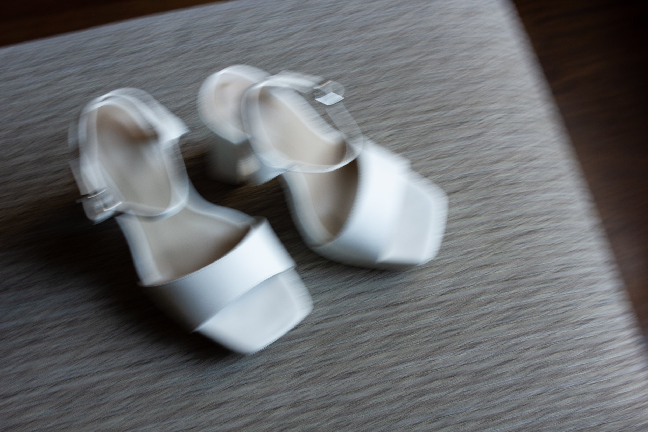A pair of white high-heeled shoes with ankle straps on a textured gray surface.