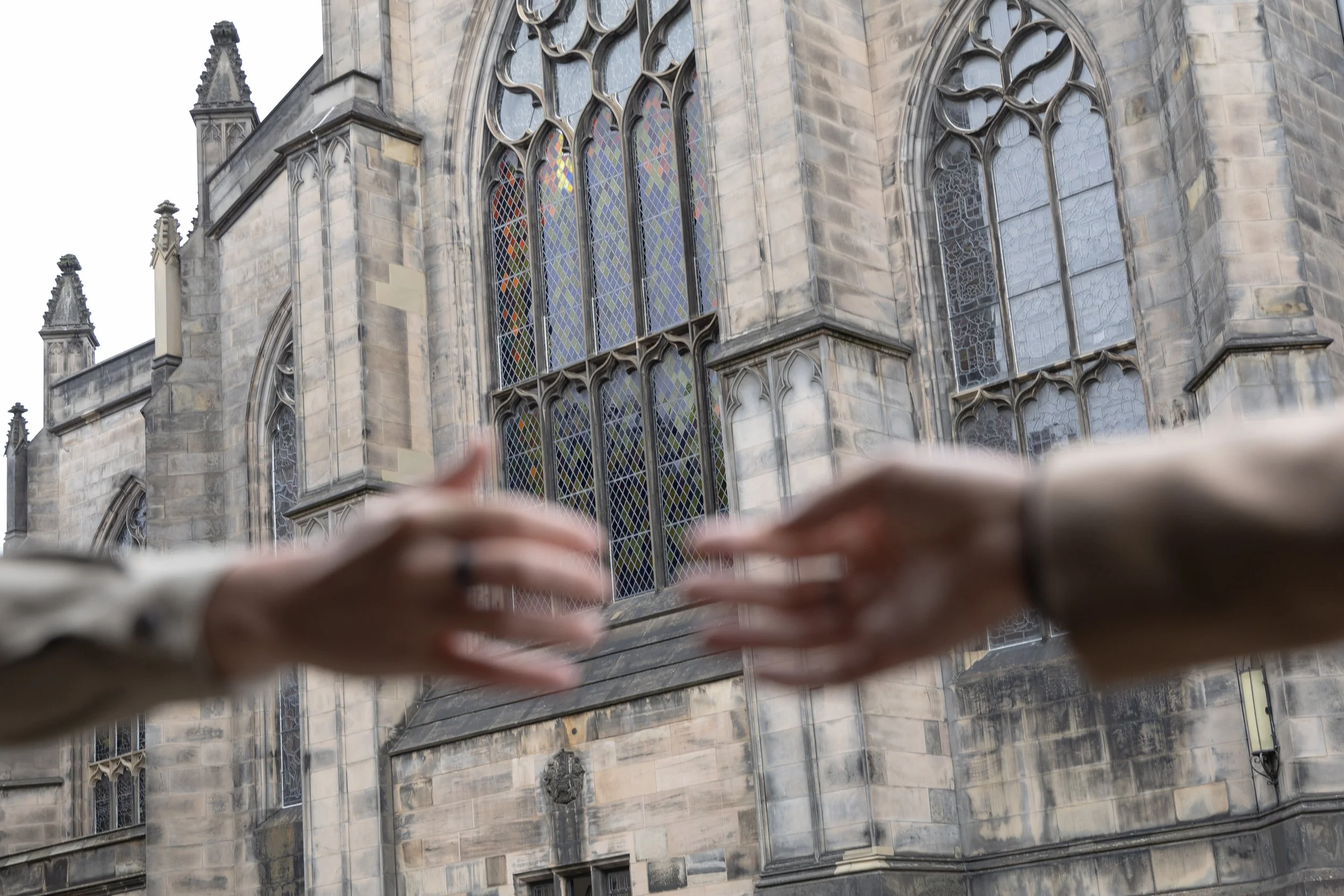 Close-up of two blurred hands reaching towards each other in front of a Gothic-style church with stained glass windows, which is St Giles cathedral located at the Royal Mile in Edinburgh, Scotland