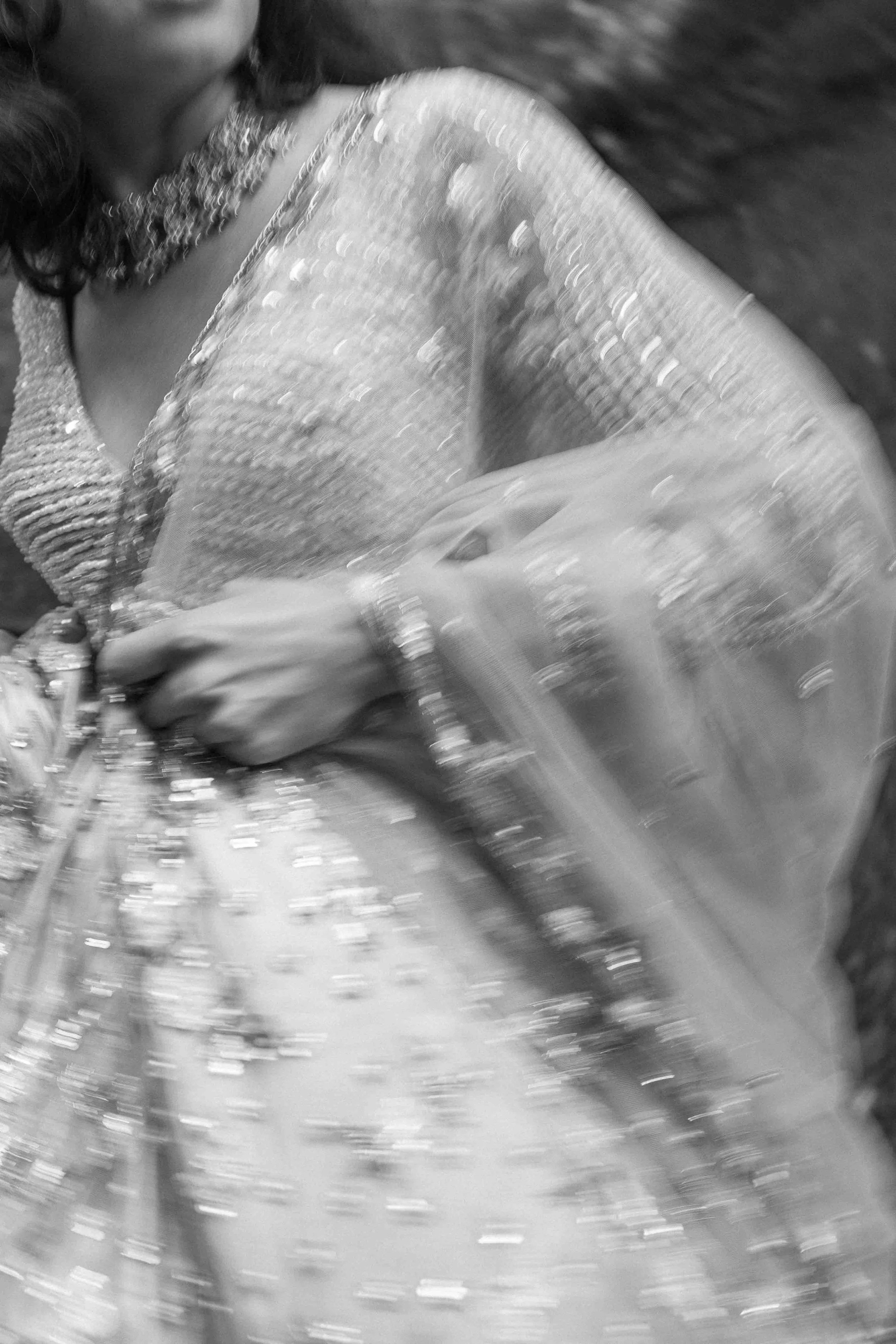 A woman in traditional Indian attire, wearing jewelry and a heavily embellished saree, draped over her shoulder with a blurred background.