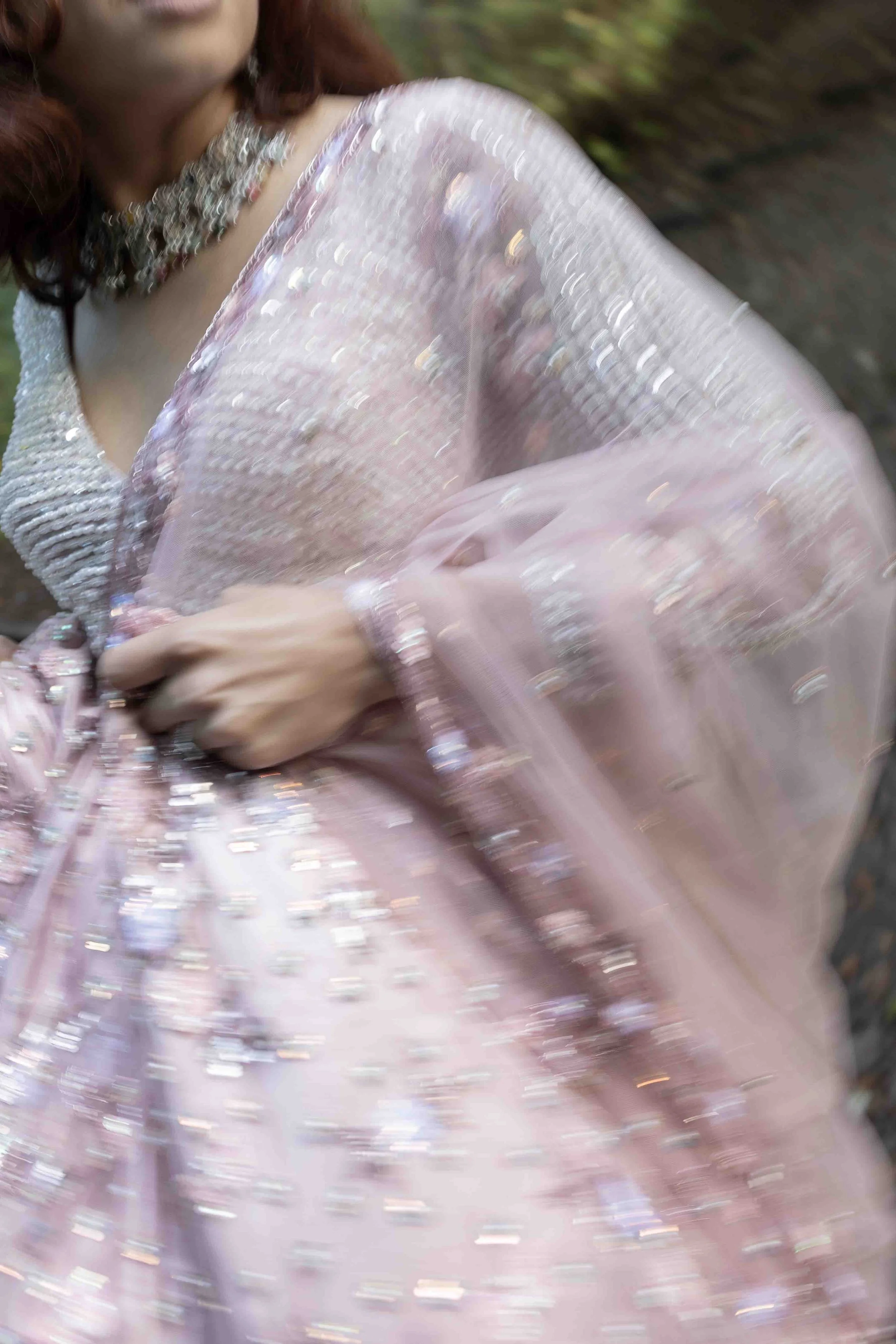 A woman in a pink, sparkly dress with beads and sequins, wearing a pearl necklace.