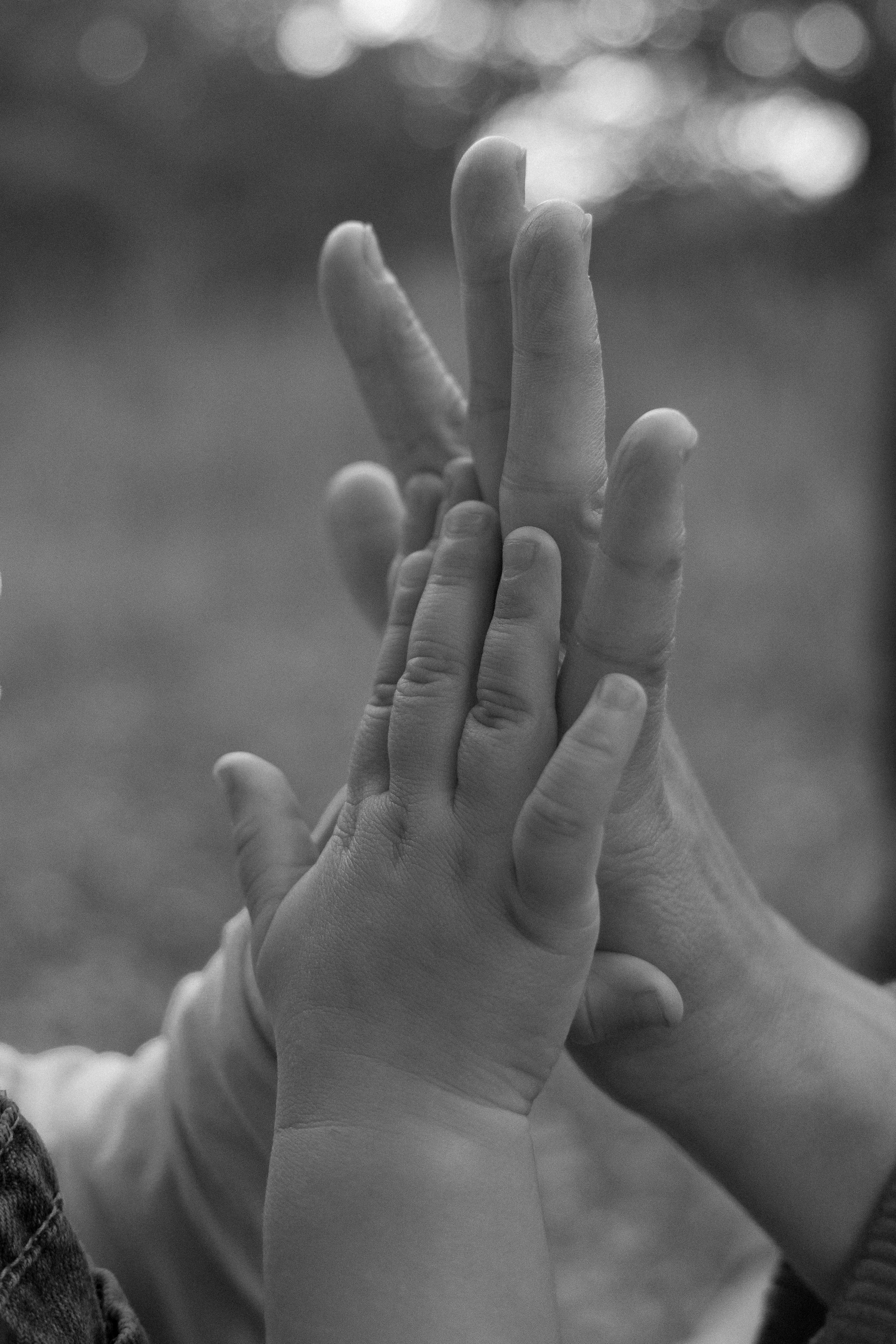 Black and white photo of multiple hands stacked on top of each other, representing unity or teamwork.