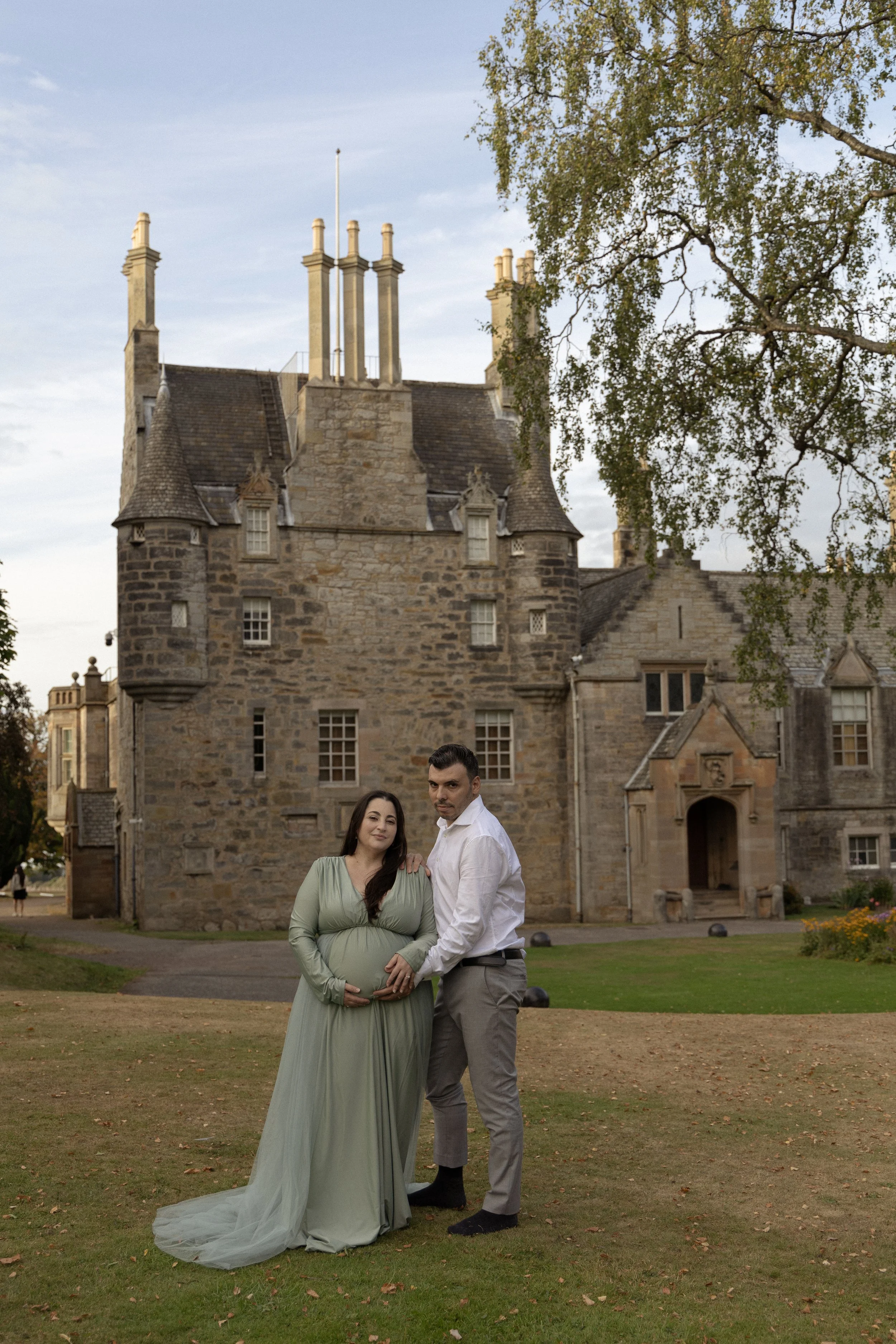 A couple stand outside in front of Lauriston Castlo, holding her belly together.