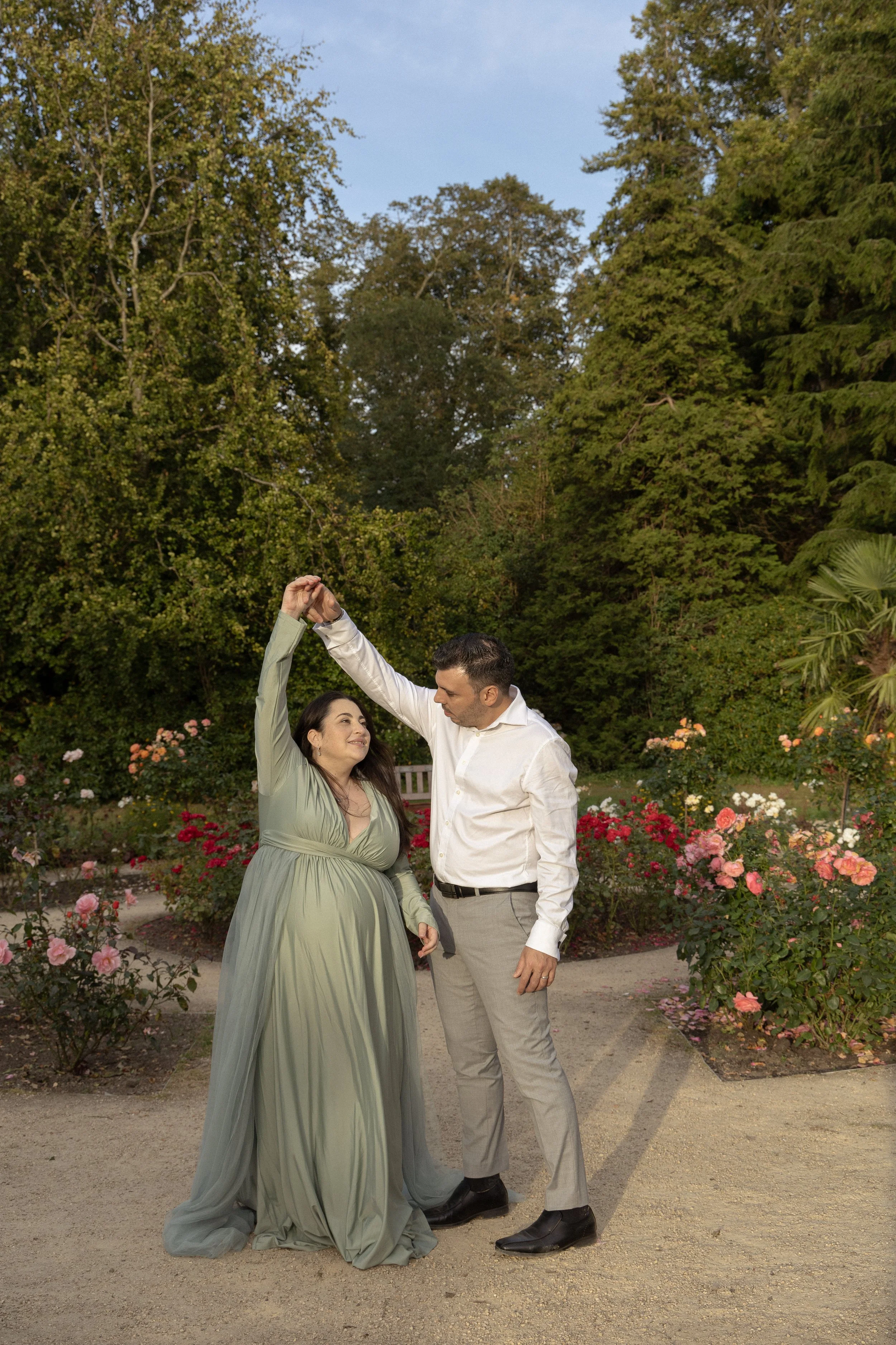 A man and woman dancing outdoors in a garden with blooming roses and lush green trees.