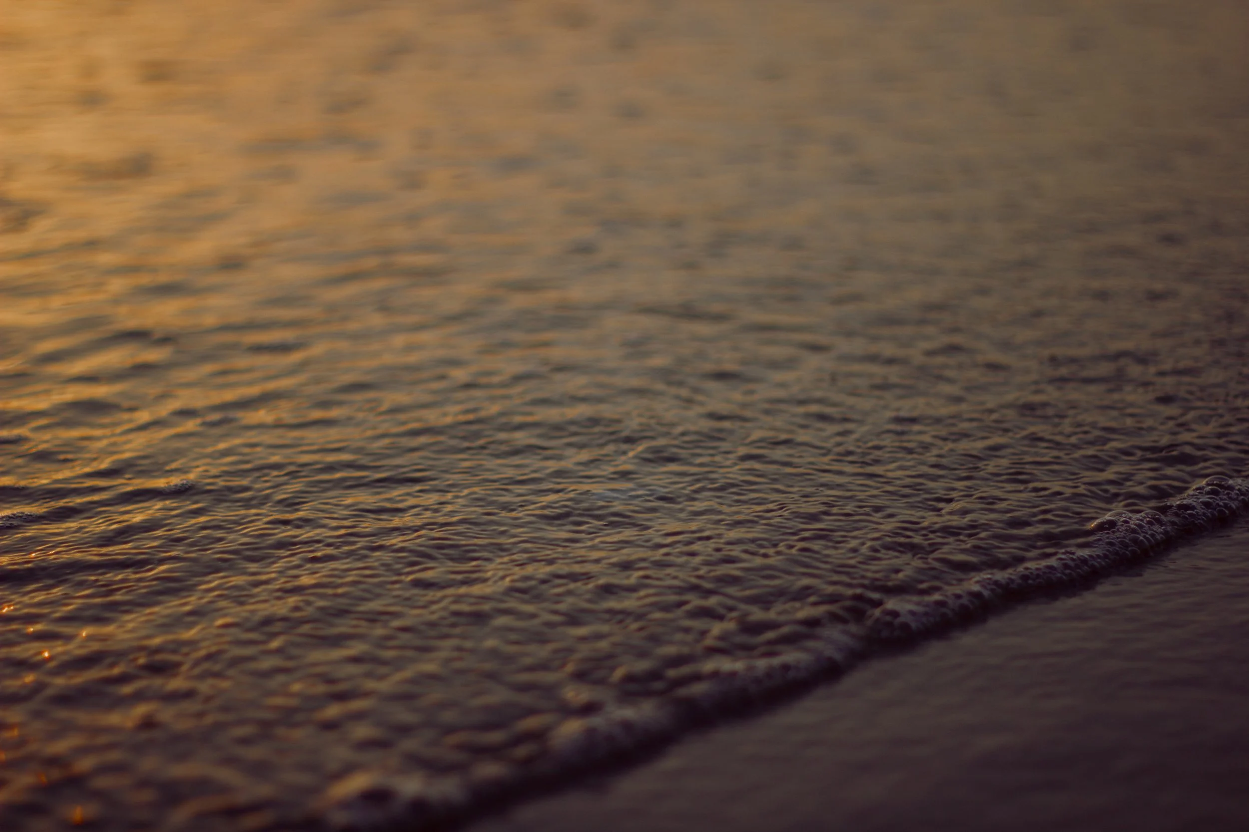 Close-up of ocean waves at sunset with orange and purple hues.