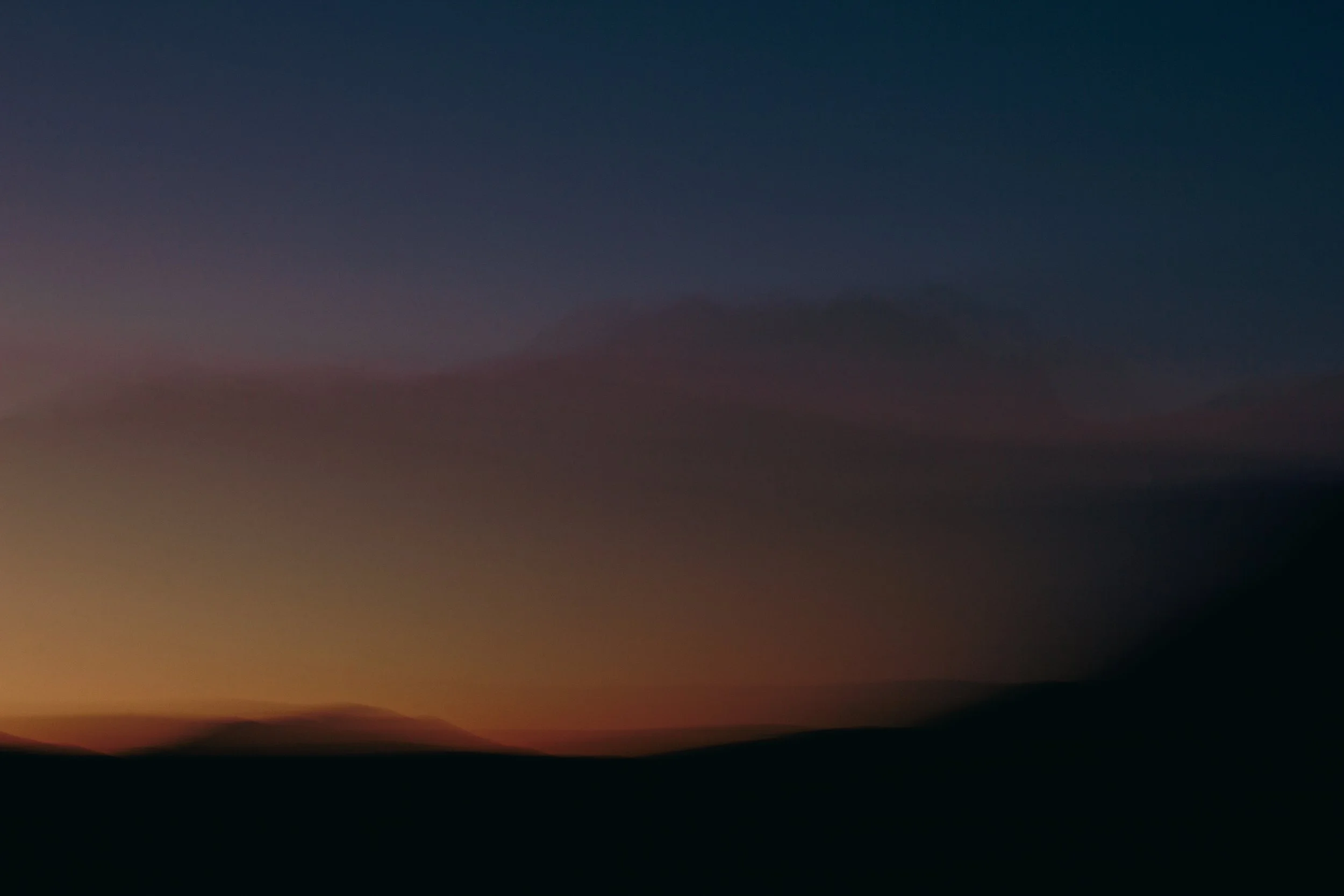A blurred sunset or sunrise sky with dark silhouette landscape.